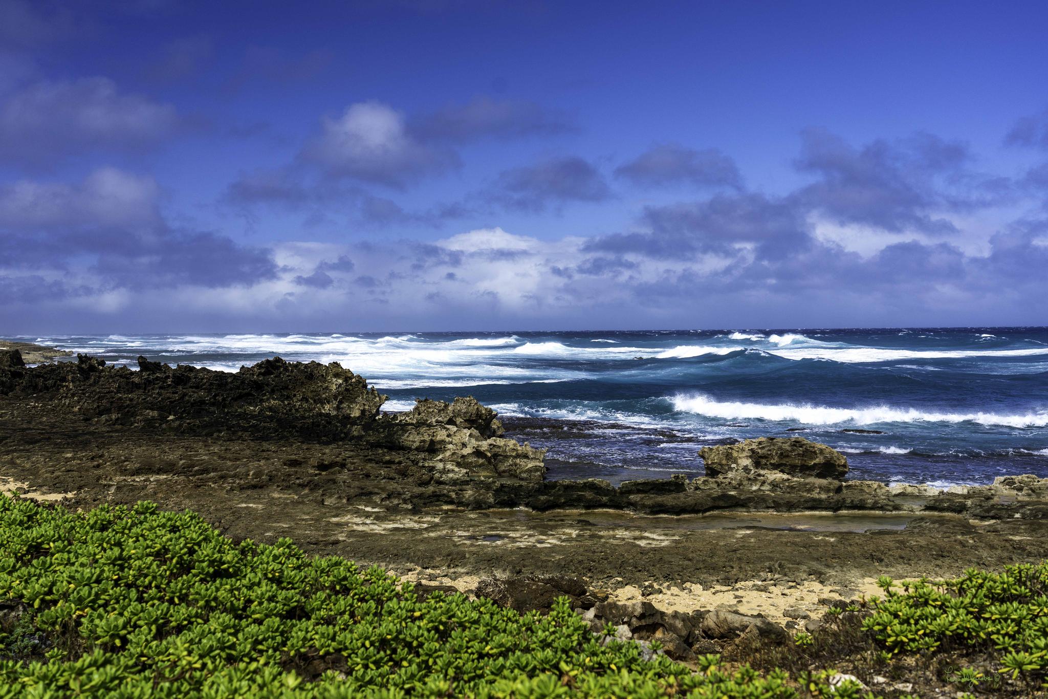 Rocky coastline with crashing waves under a dramatic, cloudy blue sky.