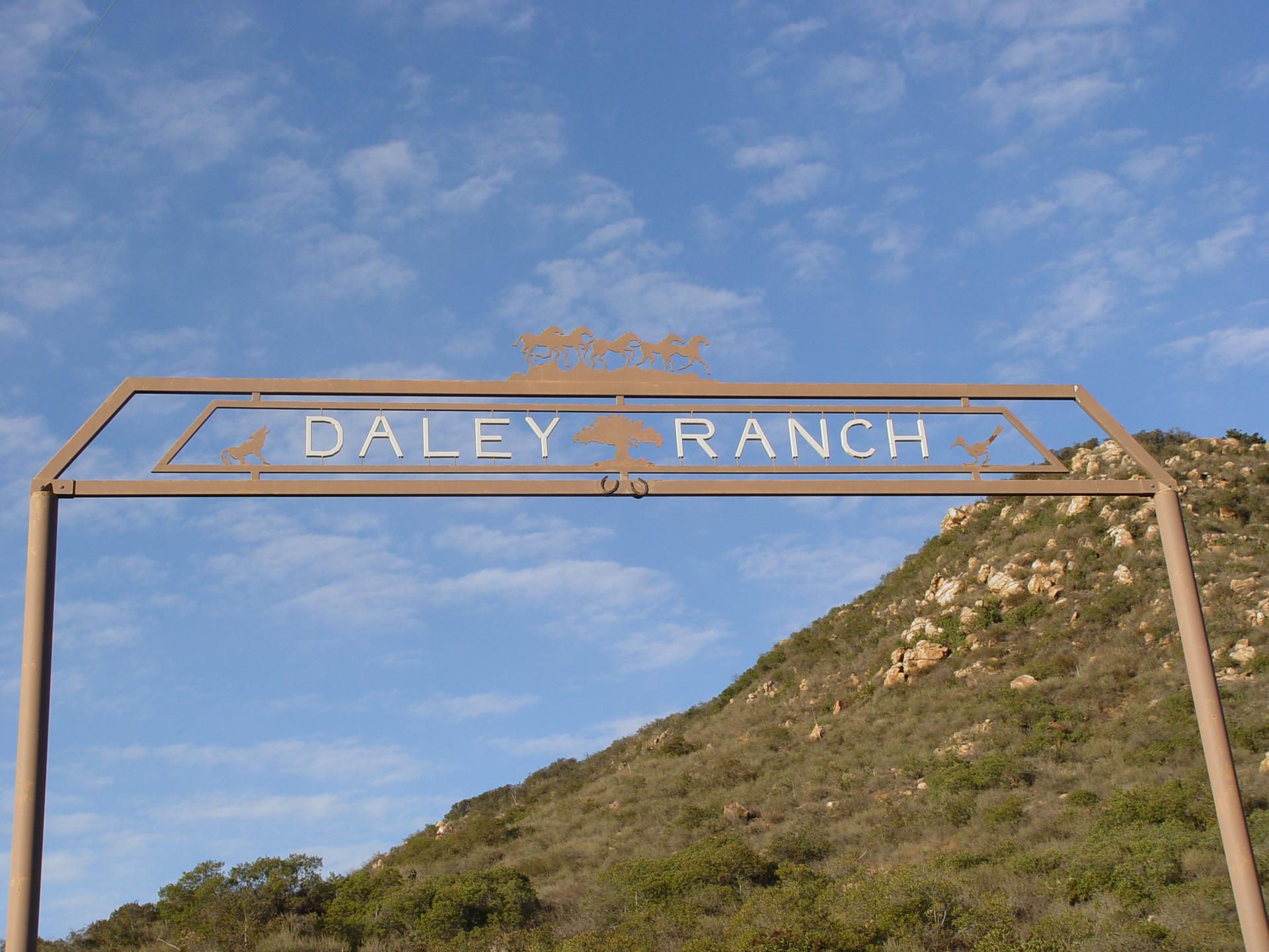 Metal archway sign against a blue sky and a rocky hillside.