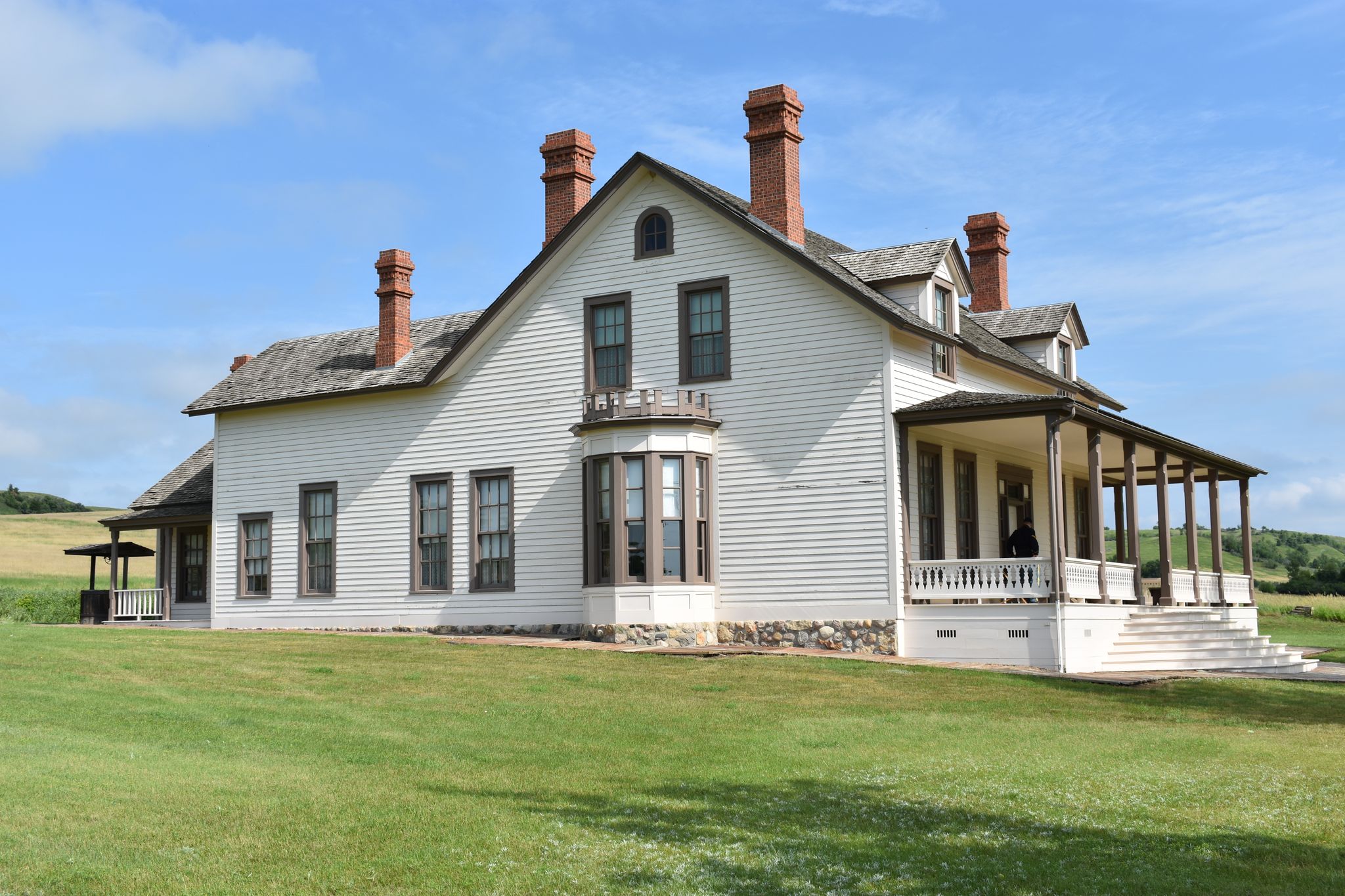 White house with multiple chimneys and a porch on a sunny green hill. - Calvary Post loop