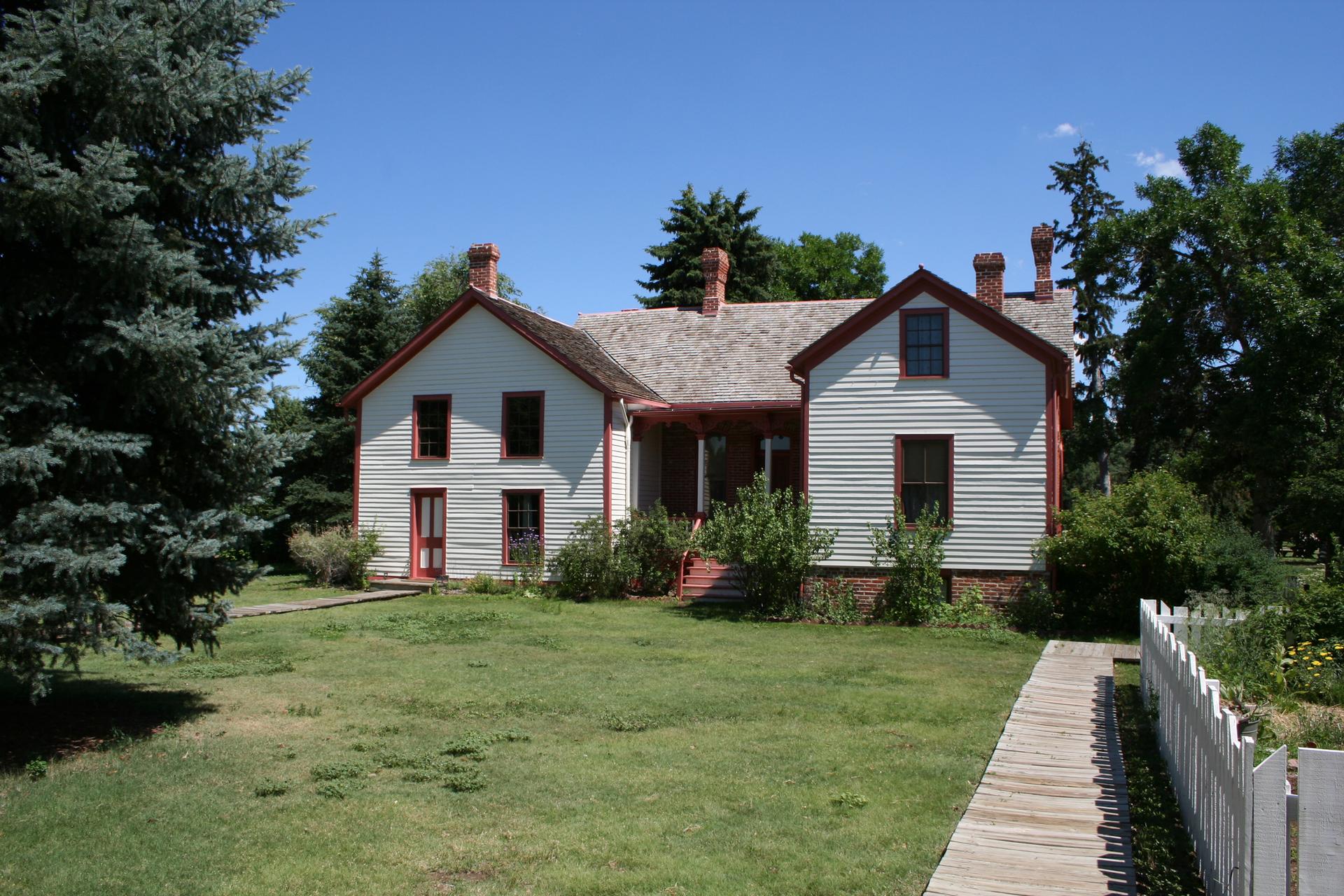 A historic white house with red trim, green lawn, and tall trees.