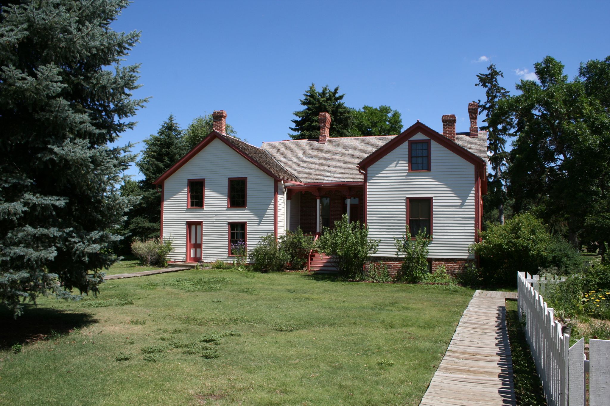 A historic white house with red trim, green lawn, and tall trees. - Cherry Creek Loop from Four Mile House Park