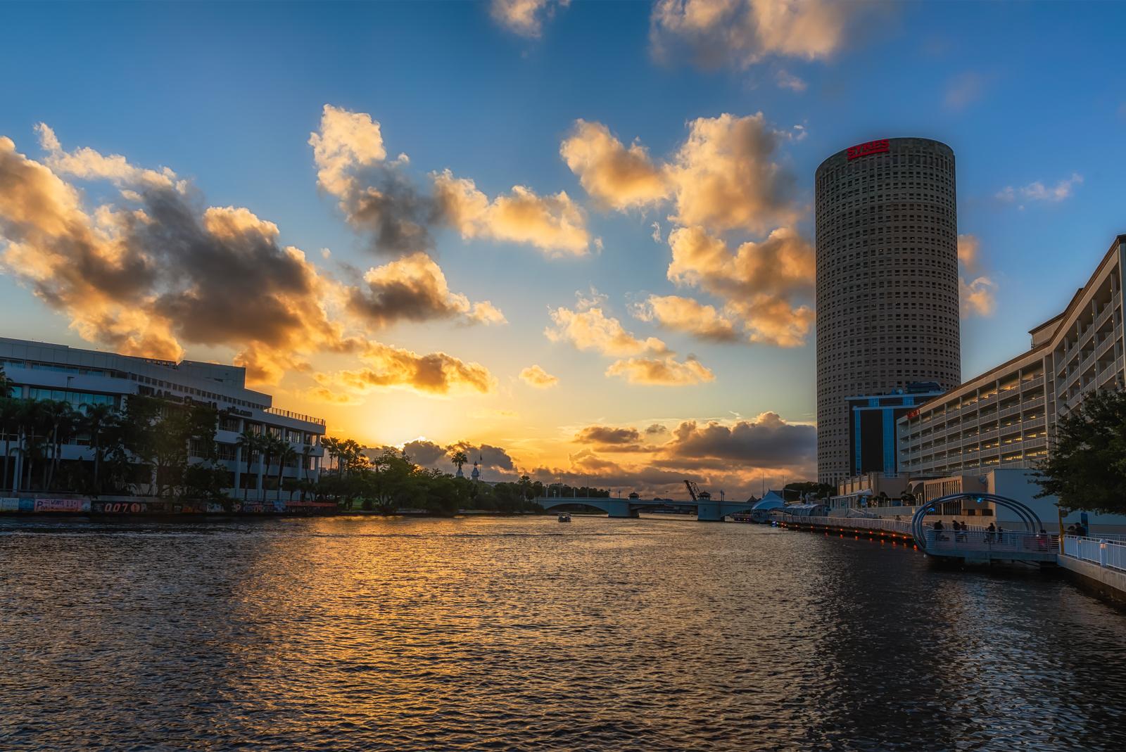 Golden sunset over a city river with a prominent cylindrical building.