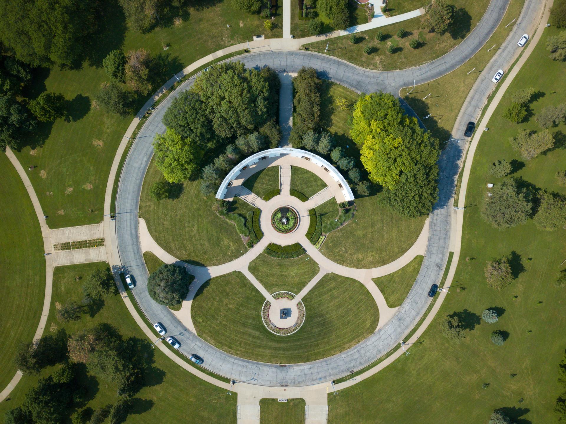 Aerial view of a circular park with roads, green trees, and a white structure.