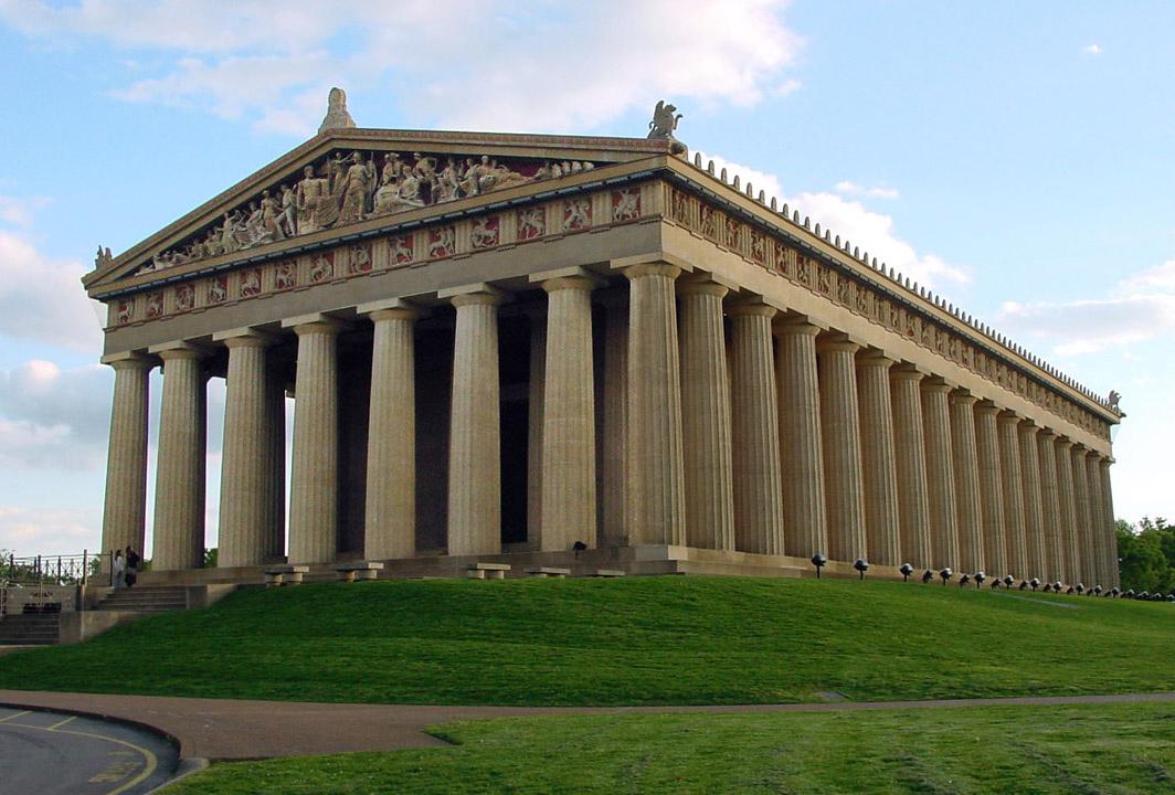 A large classical temple with many columns sits on a green hill.