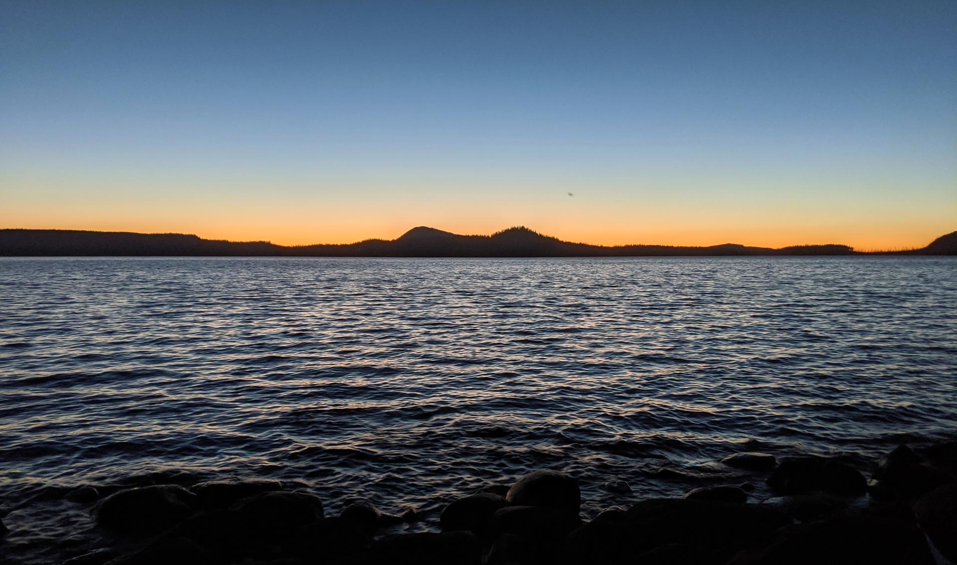 Dark water and silhouetted mountains under an orange and blue sunset sky.