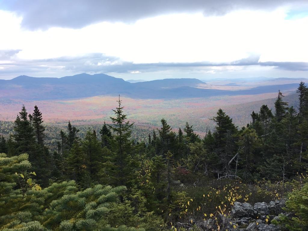 Vast mountain landscape with autumn-colored valley under an overcast sky.
