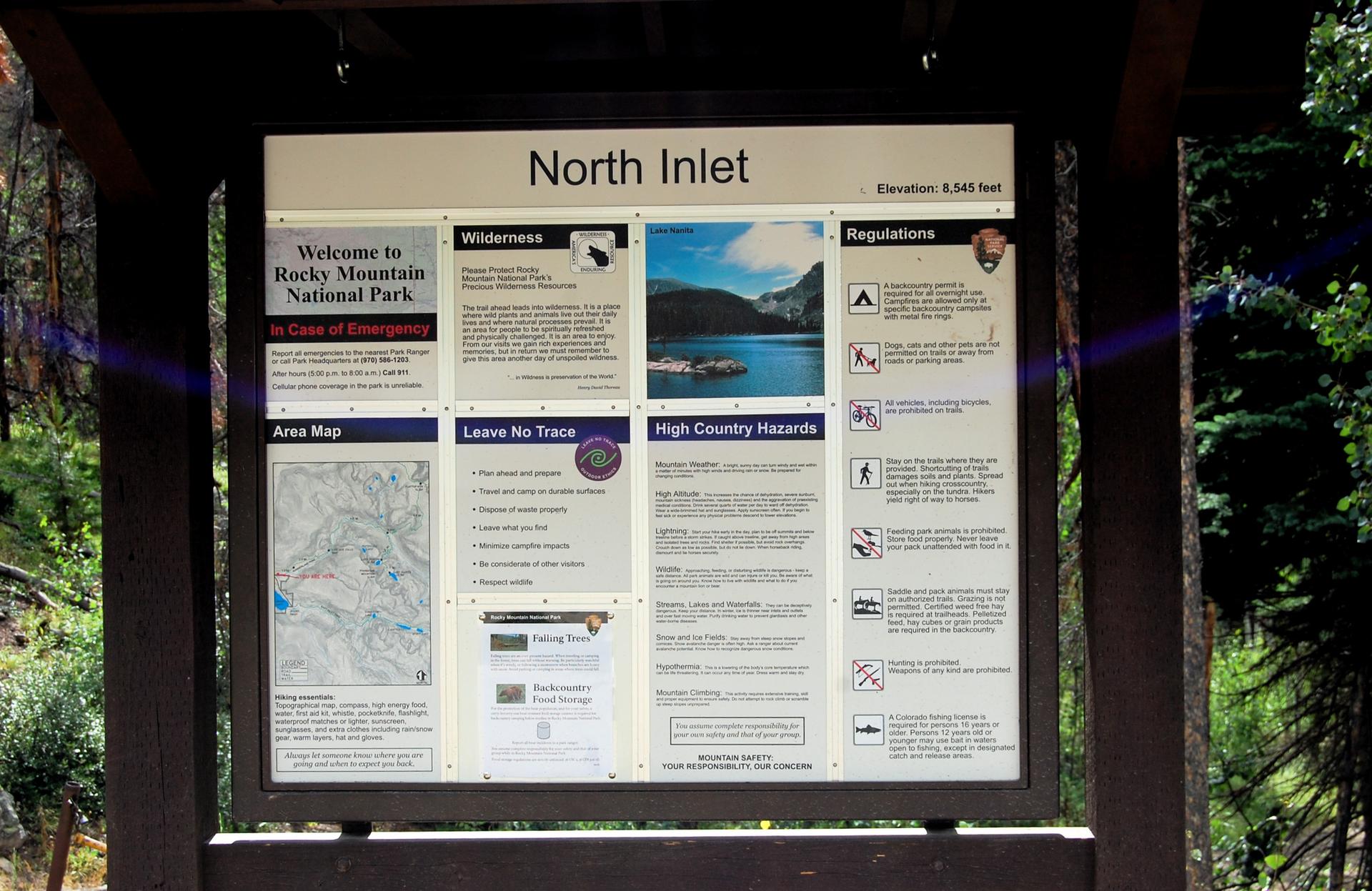 Large information sign with maps and regulations in a shaded forest.