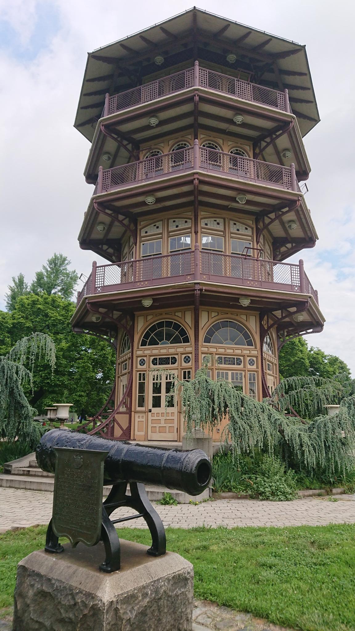 A tall, ornate pagoda building with a cannon in the foreground under bright skies.