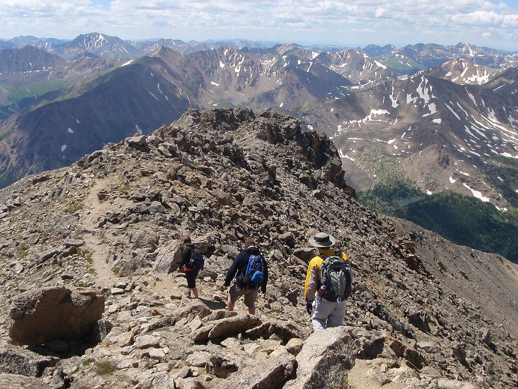 Three hikers traverse a rocky mountain ridge under a bright sky. - Mount Massive Southwest Slopes Trail