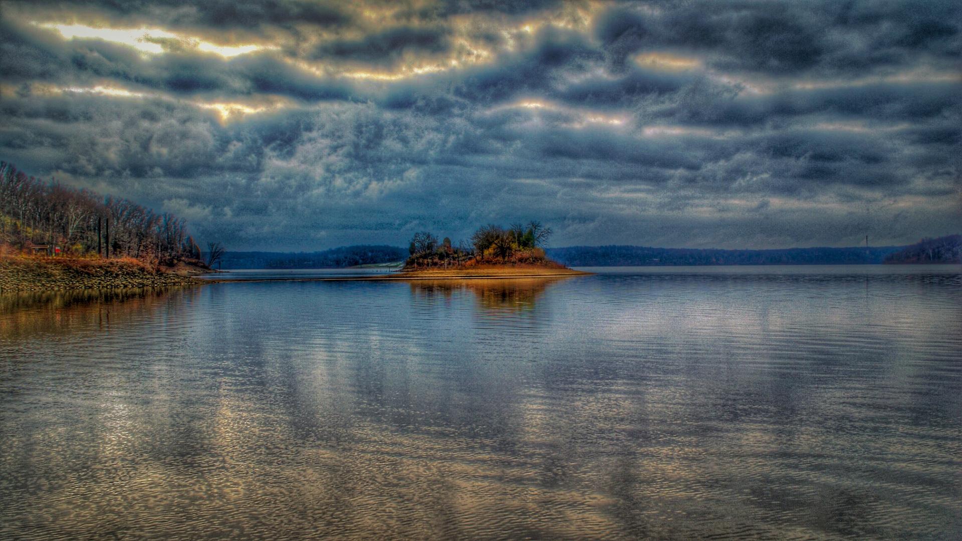 A wide lake under a dramatic, cloudy sky with a small island.