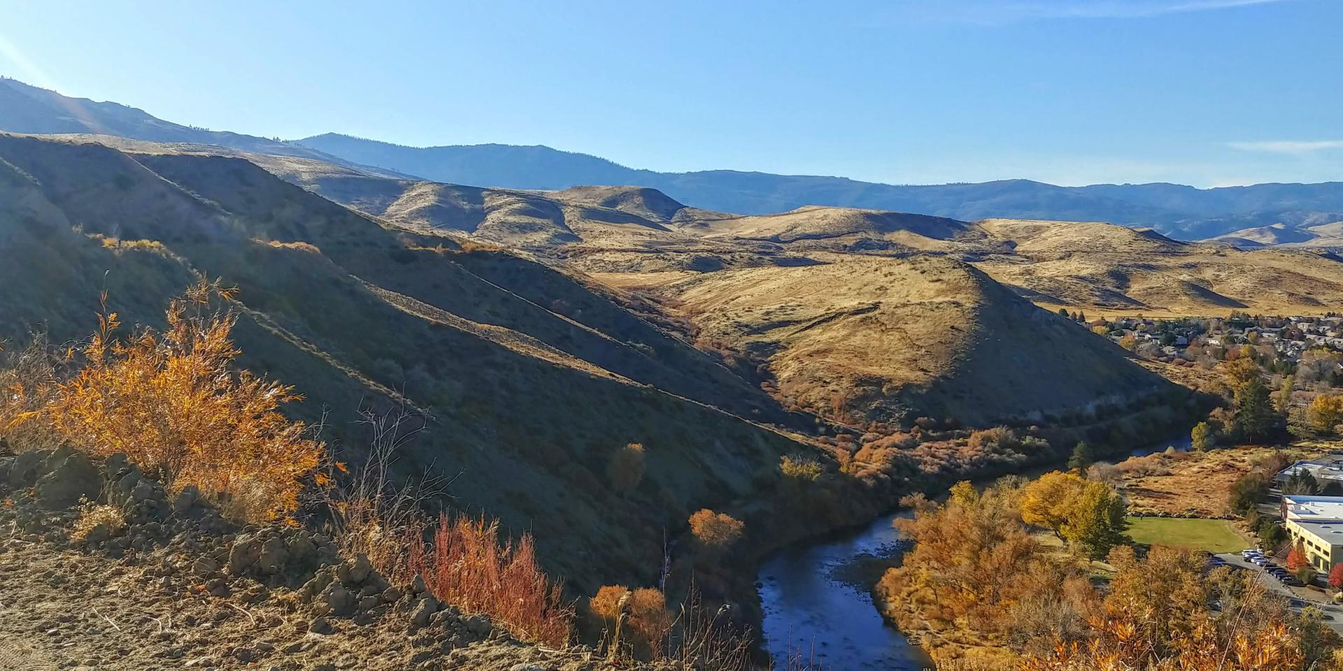 Sunny view of a river winding through dry, rolling hills with fall foliage.