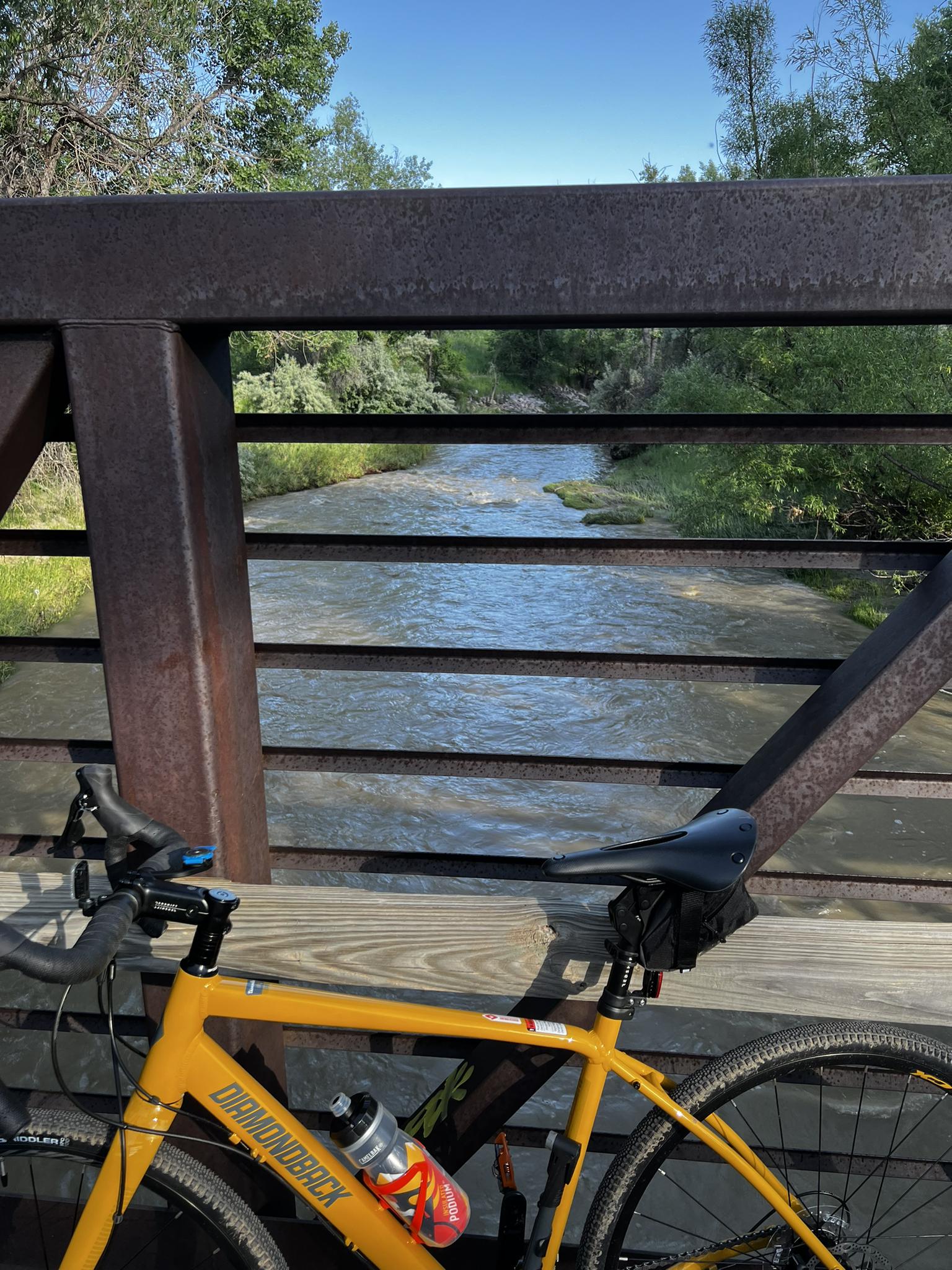 Yellow bicycle on a rusty bridge overlooking a flowing river in bright daylight.