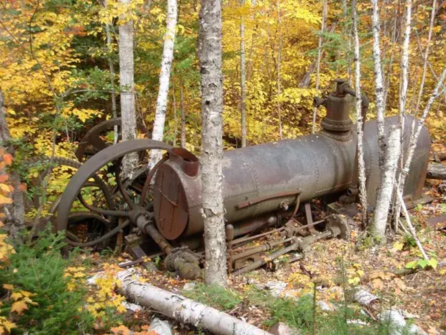 Rusty old machinery abandoned in a vibrant autumn forest with yellow and orange leaves.