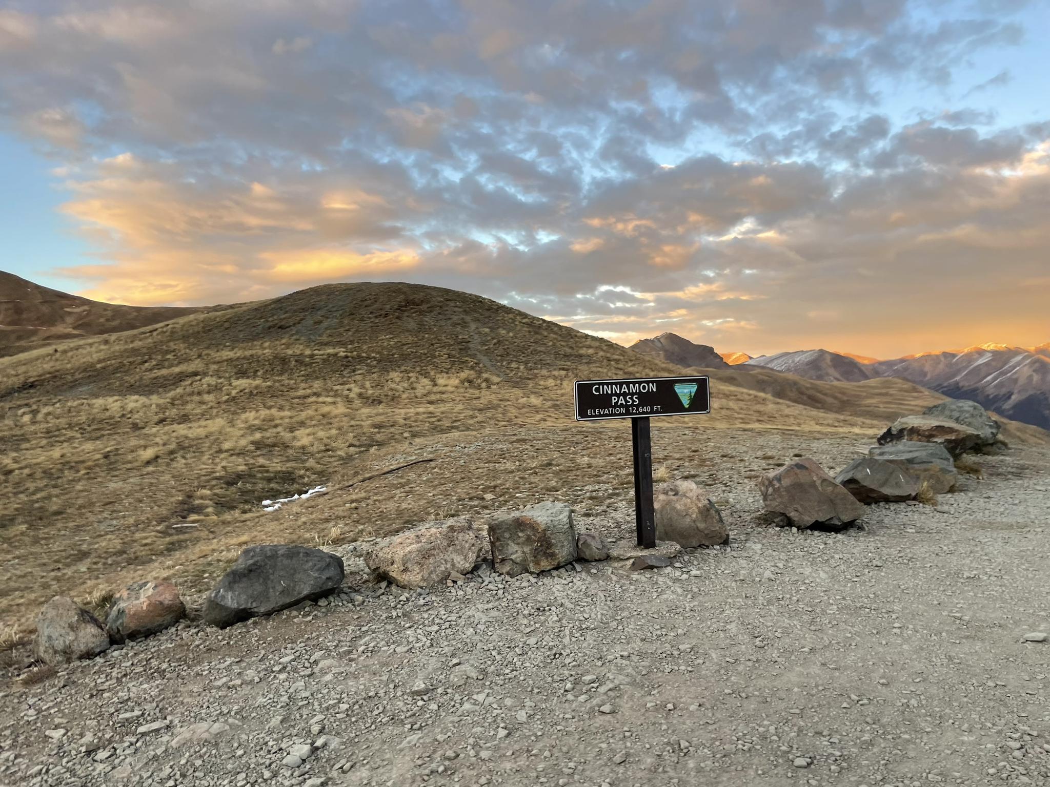 Sign on a gravel road at a mountain pass during a colorful sunset.