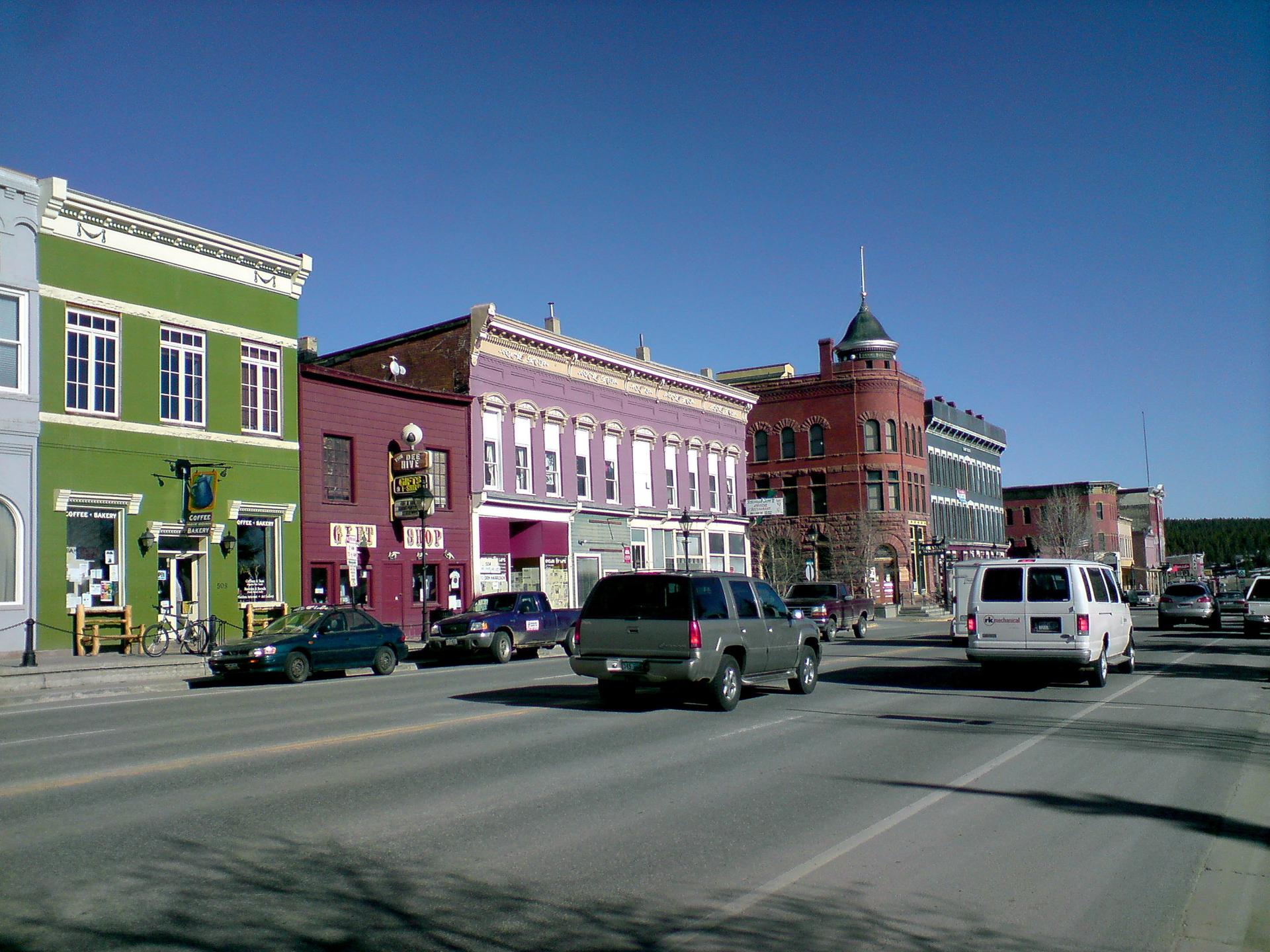Colorful historic buildings line a sunny street with cars driving.