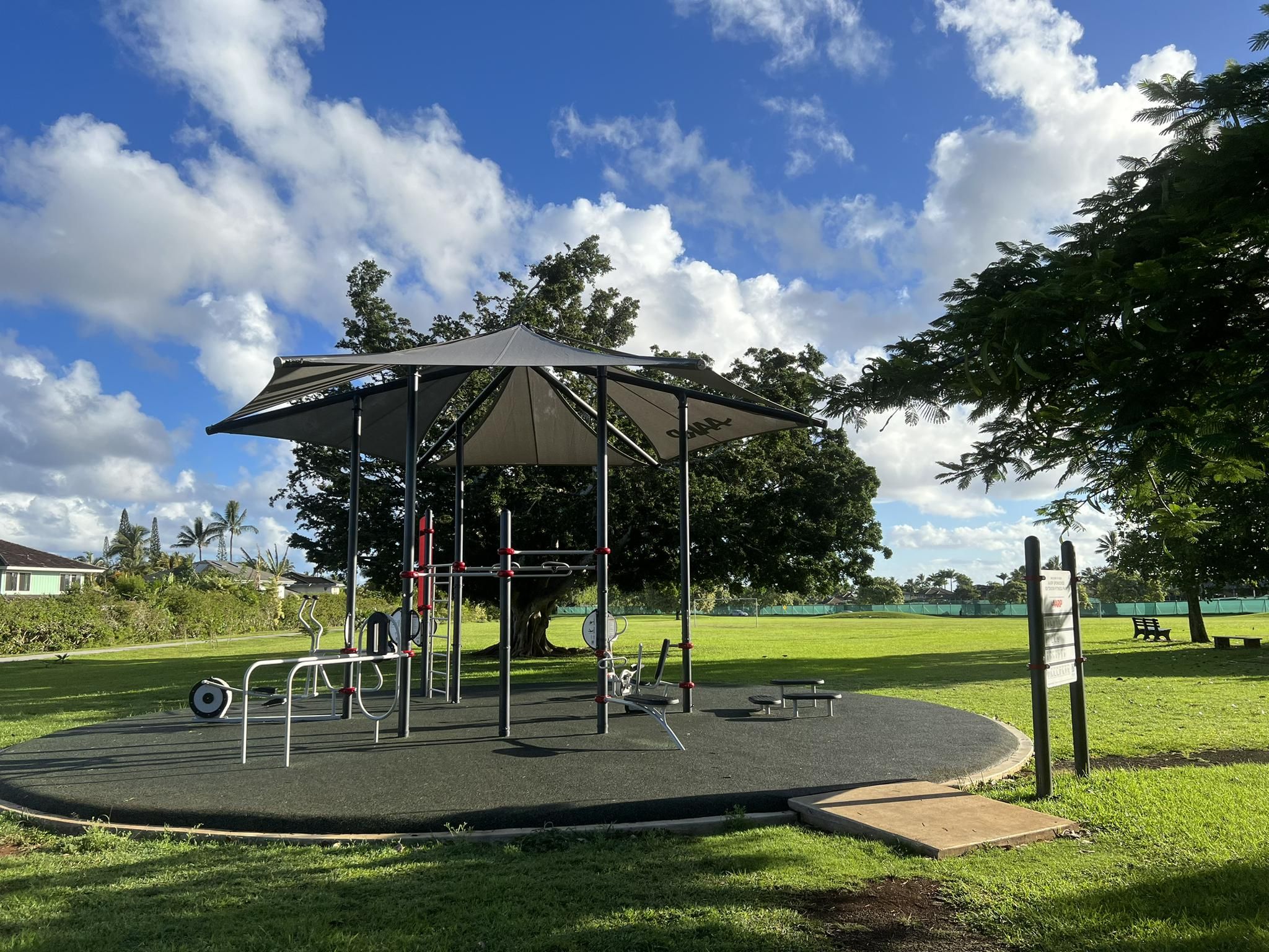 Outdoor fitness equipment under a canopy in a sunny park with green grass. - Prince Albert Park loop from Princeville