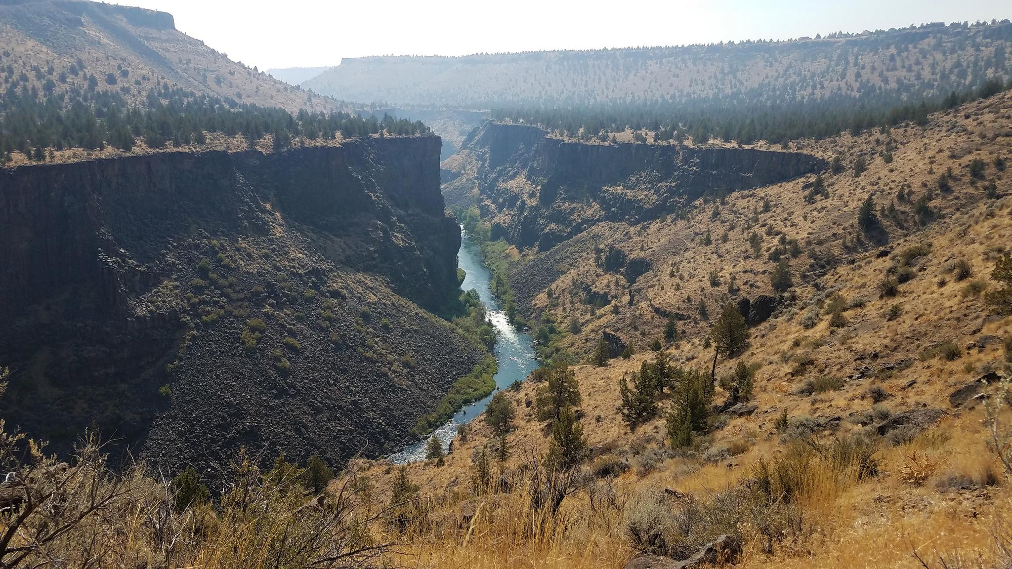 A wide river flows through a deep, sunlit canyon with rocky, dry slopes.