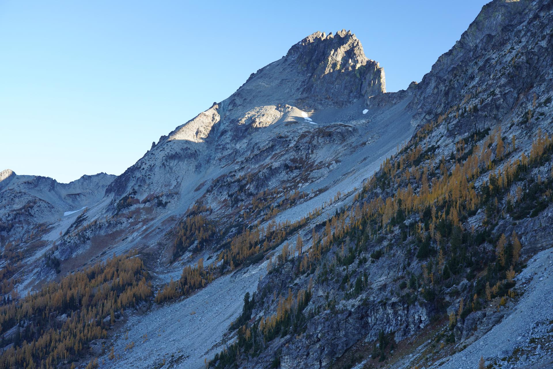 Steep, rocky mountainsides with golden trees, sunlit peaks, and clear blue sky.