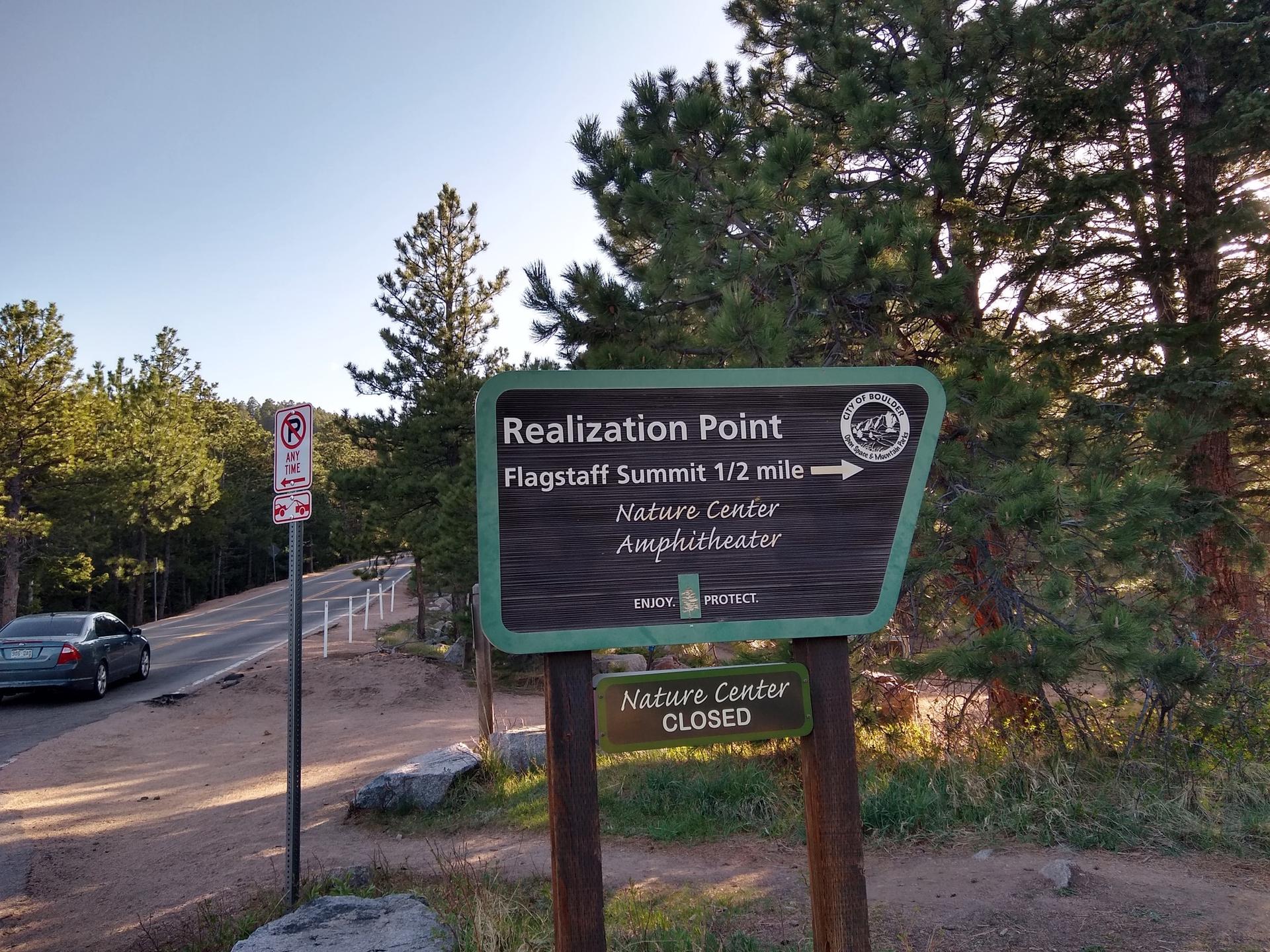 Wooden sign with directions next to a paved road and pine trees.
