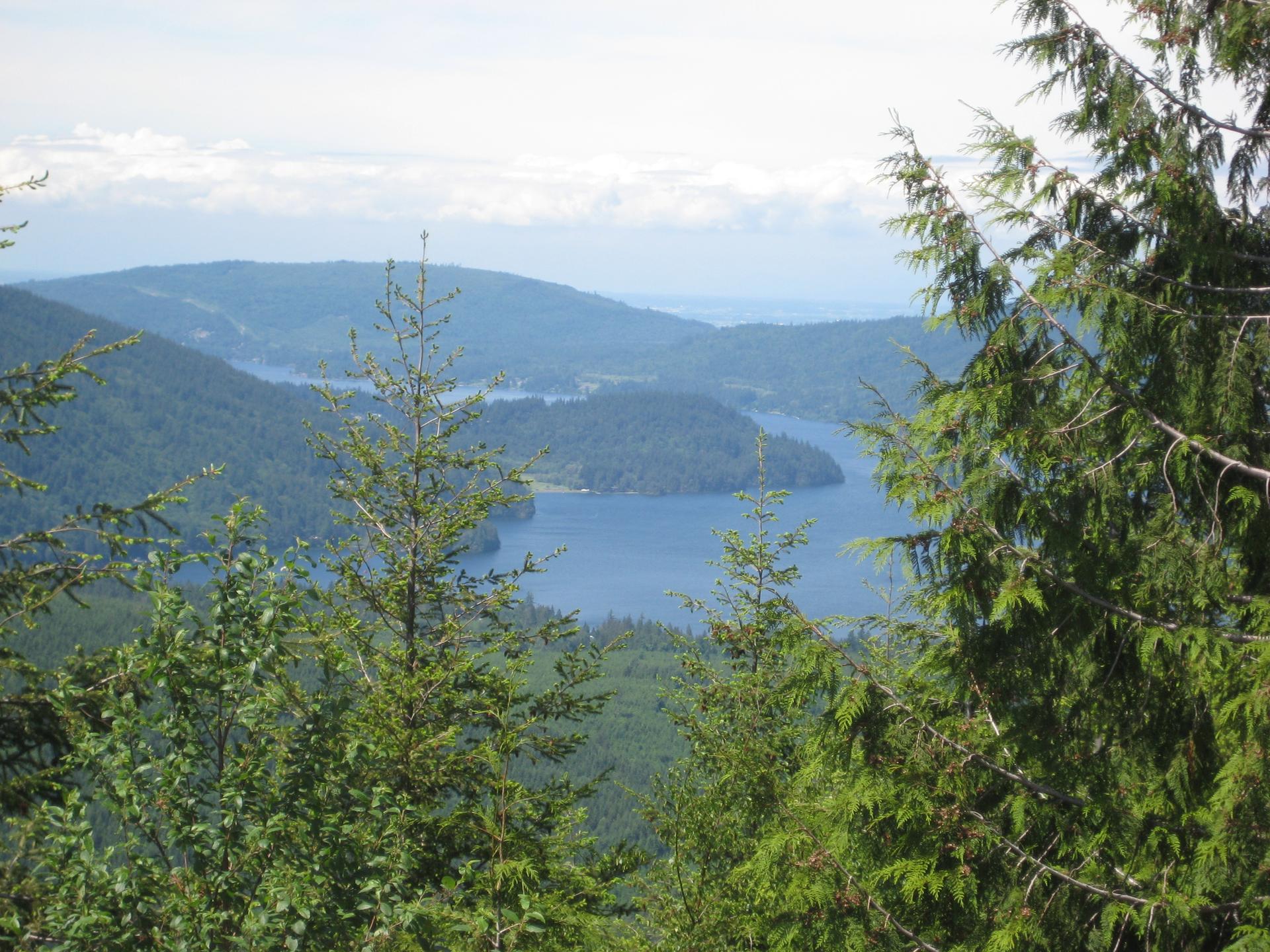 Panoramic view of a blue waterway winding through lush green forested hills under a bright sky.
