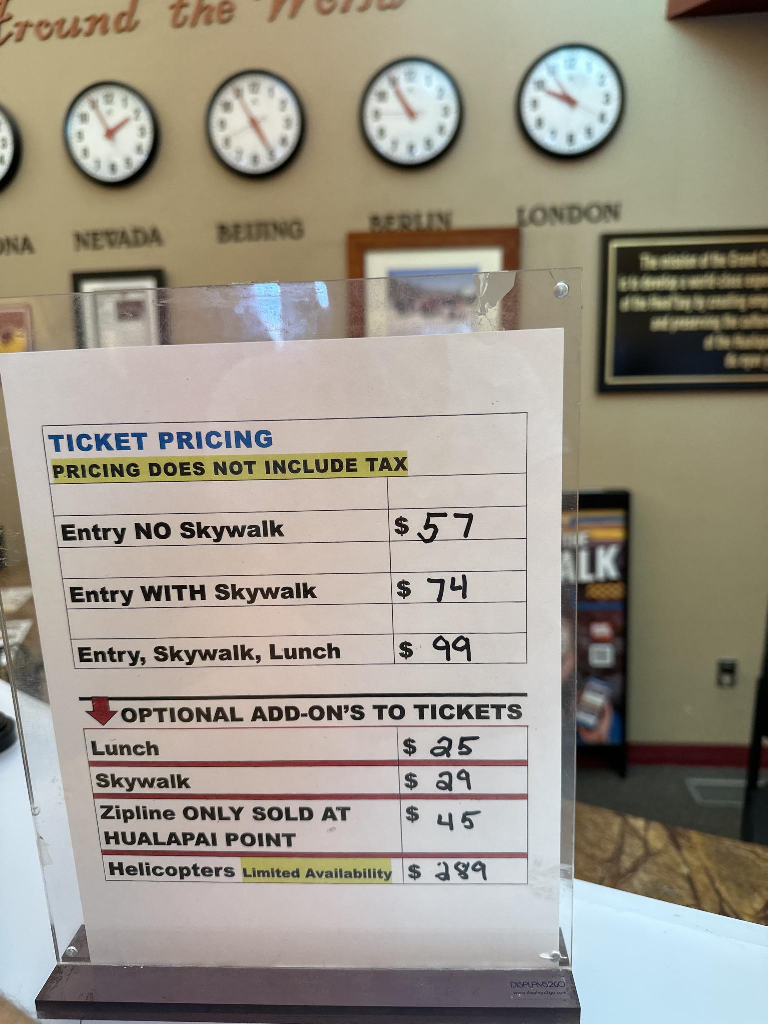 Close-up of a ticket pricing sign on a counter with multiple clocks in the background.