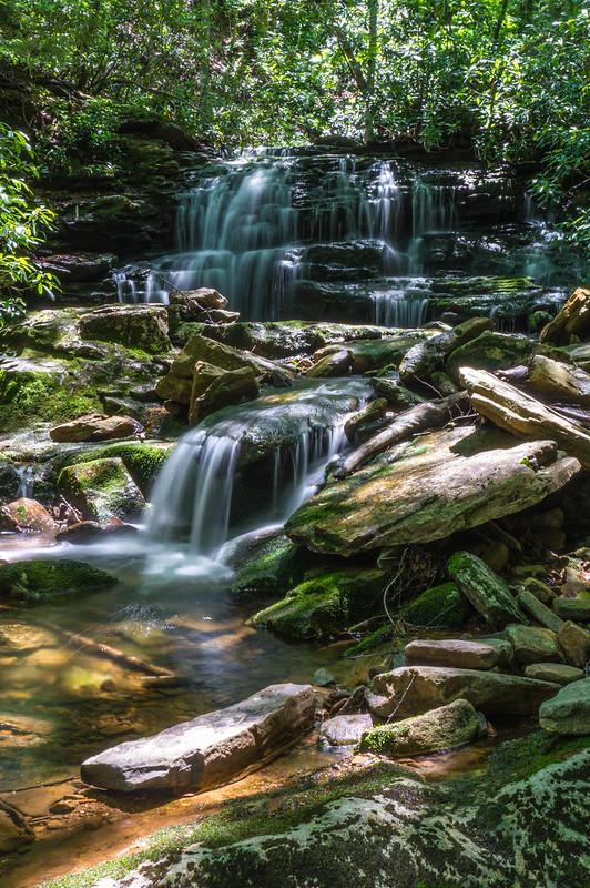 Cascading waterfall over mossy rocks in a lush green forest, dappled sunlight.