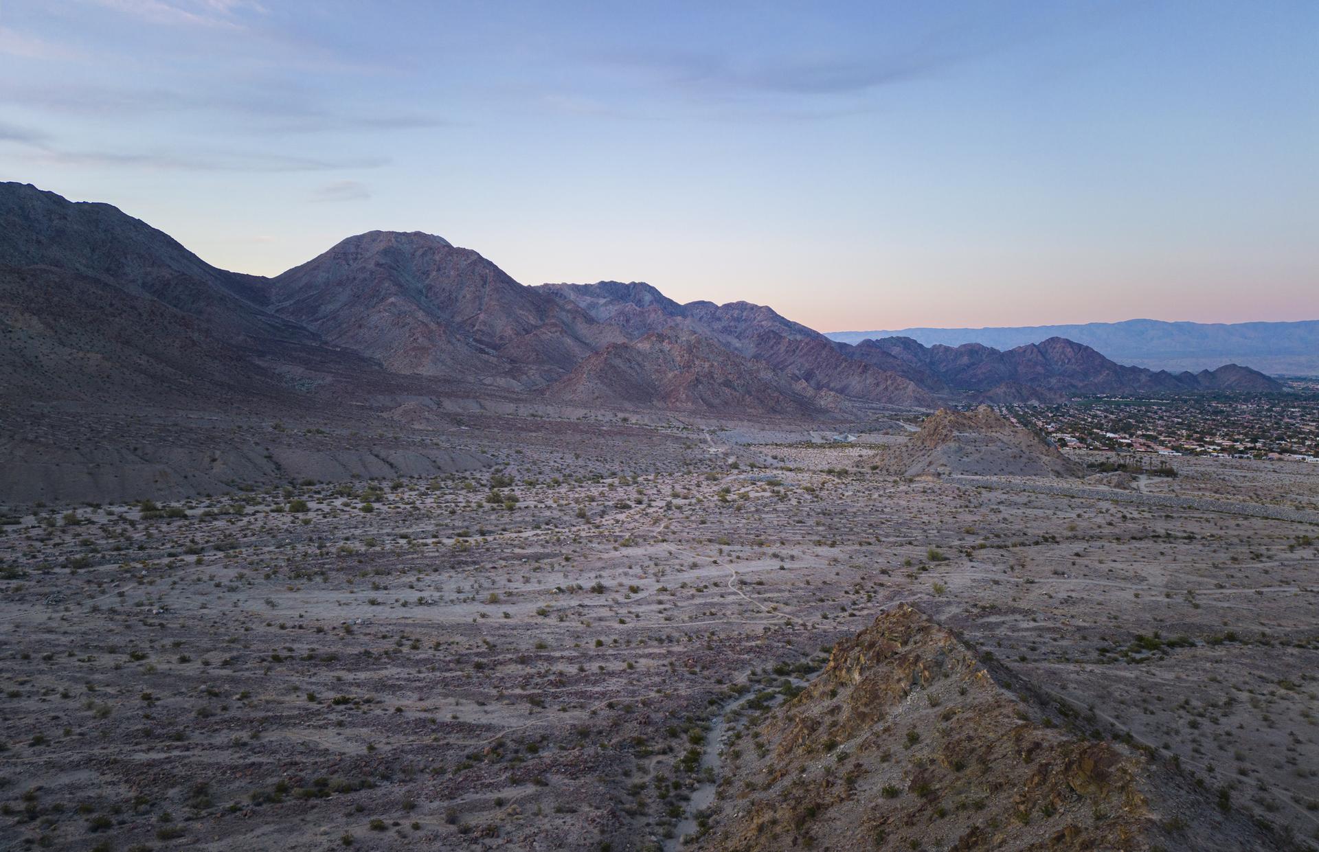 Expansive desert valley and mountains under a soft, colorful twilight sky.