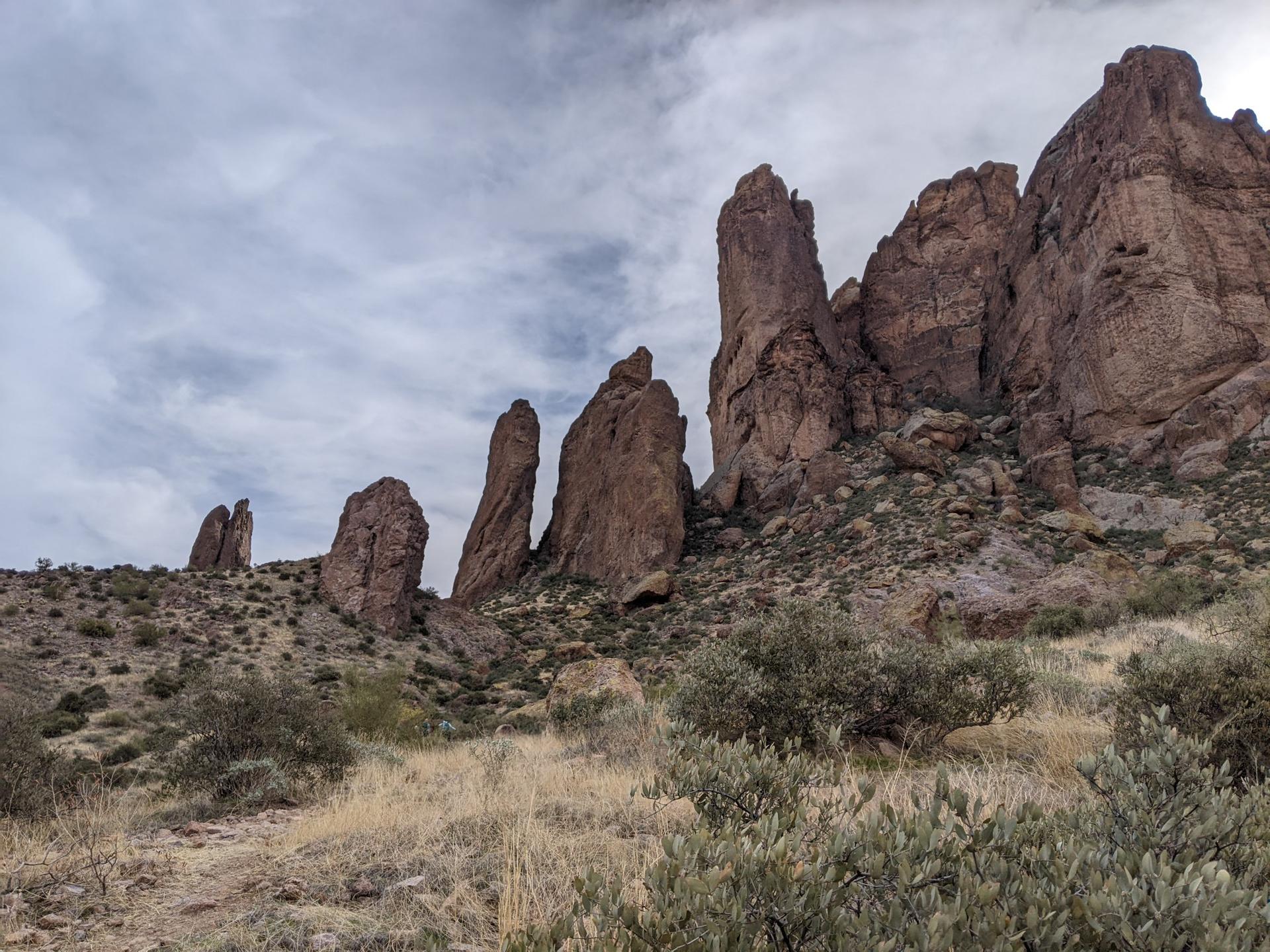 Tall rock formations rise from a desert landscape under a cloudy sky.