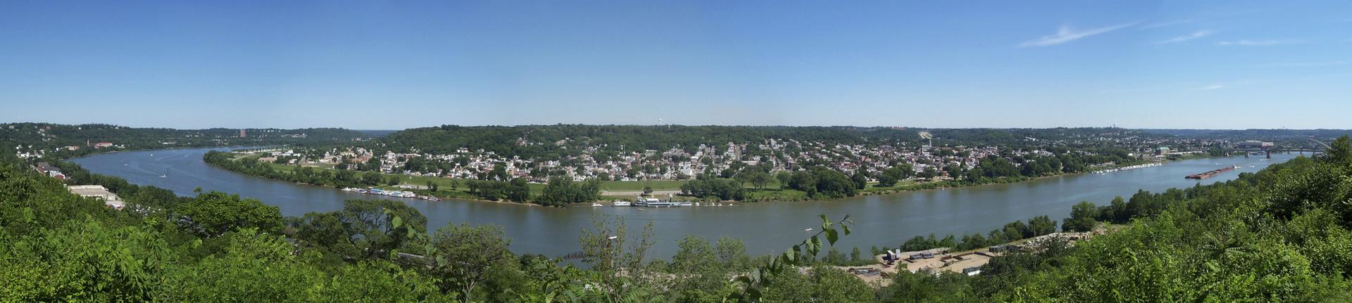Panoramic view of a wide river winding through a town on green hills.
