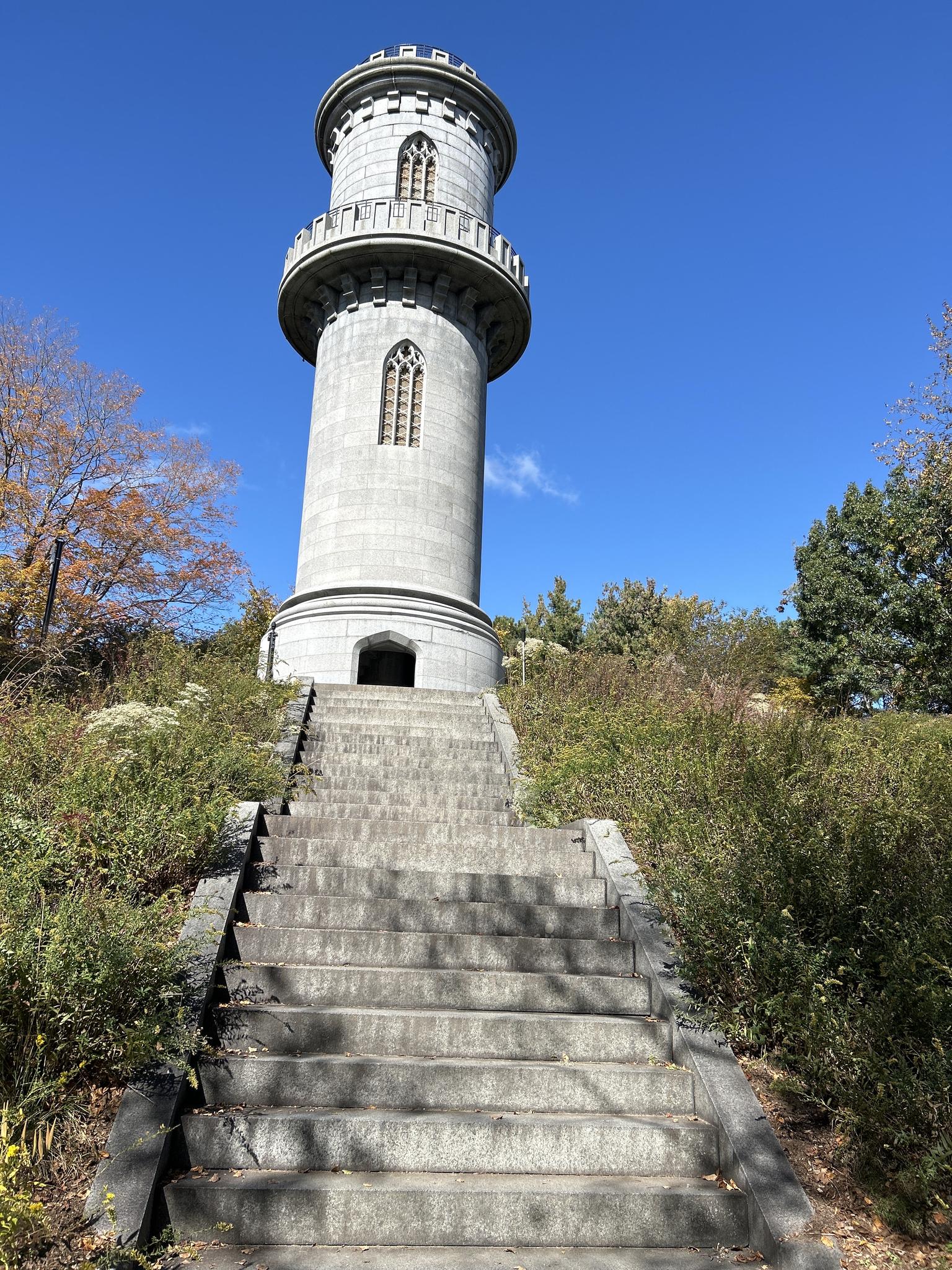 Tall, grey stone tower with a turret, approached by stone steps.