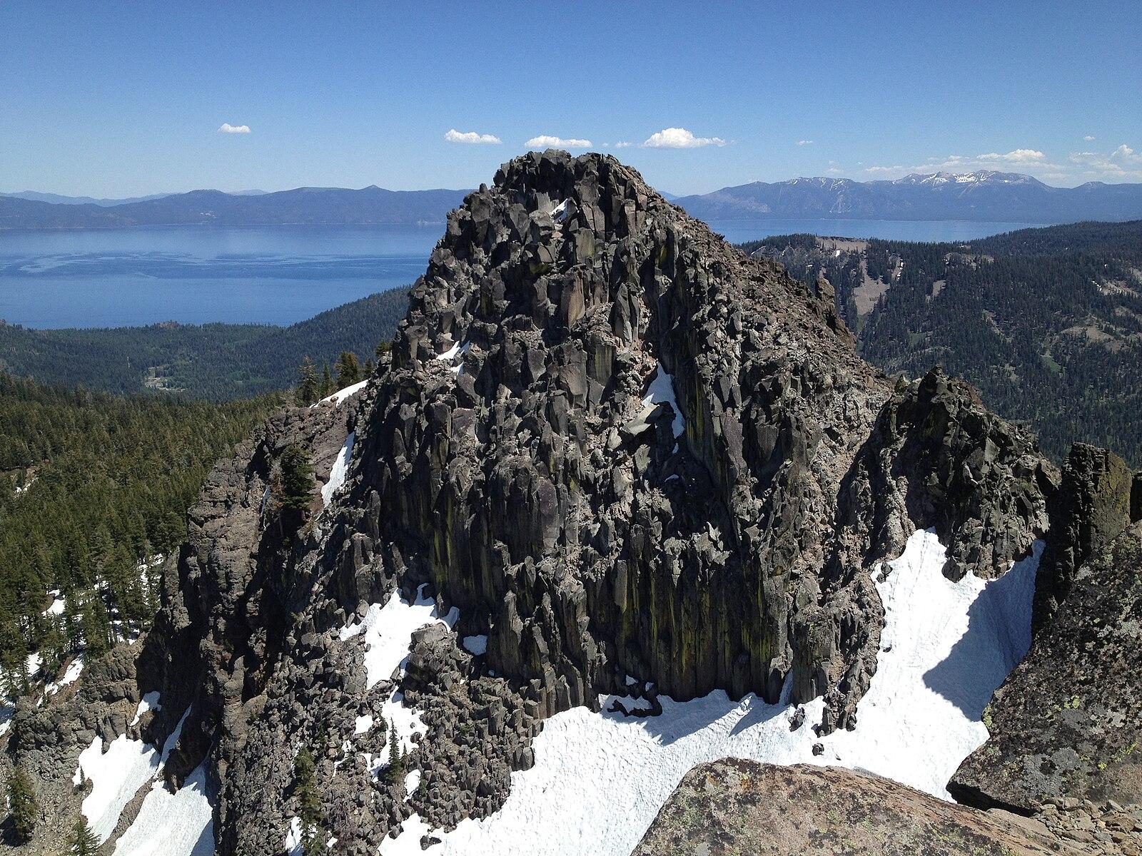 Rugged rocky peak with patches of snow under a clear blue sky.