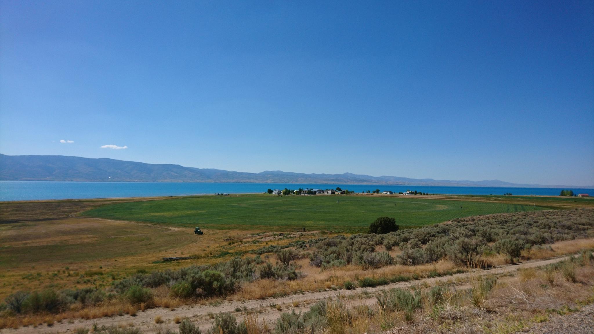 Vast landscape with green fields, turquoise water, and distant mountains under clear sky.