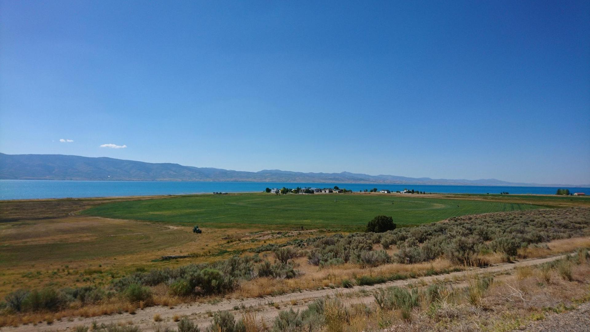 Vast landscape with green fields, turquoise water, and distant mountains under clear sky.