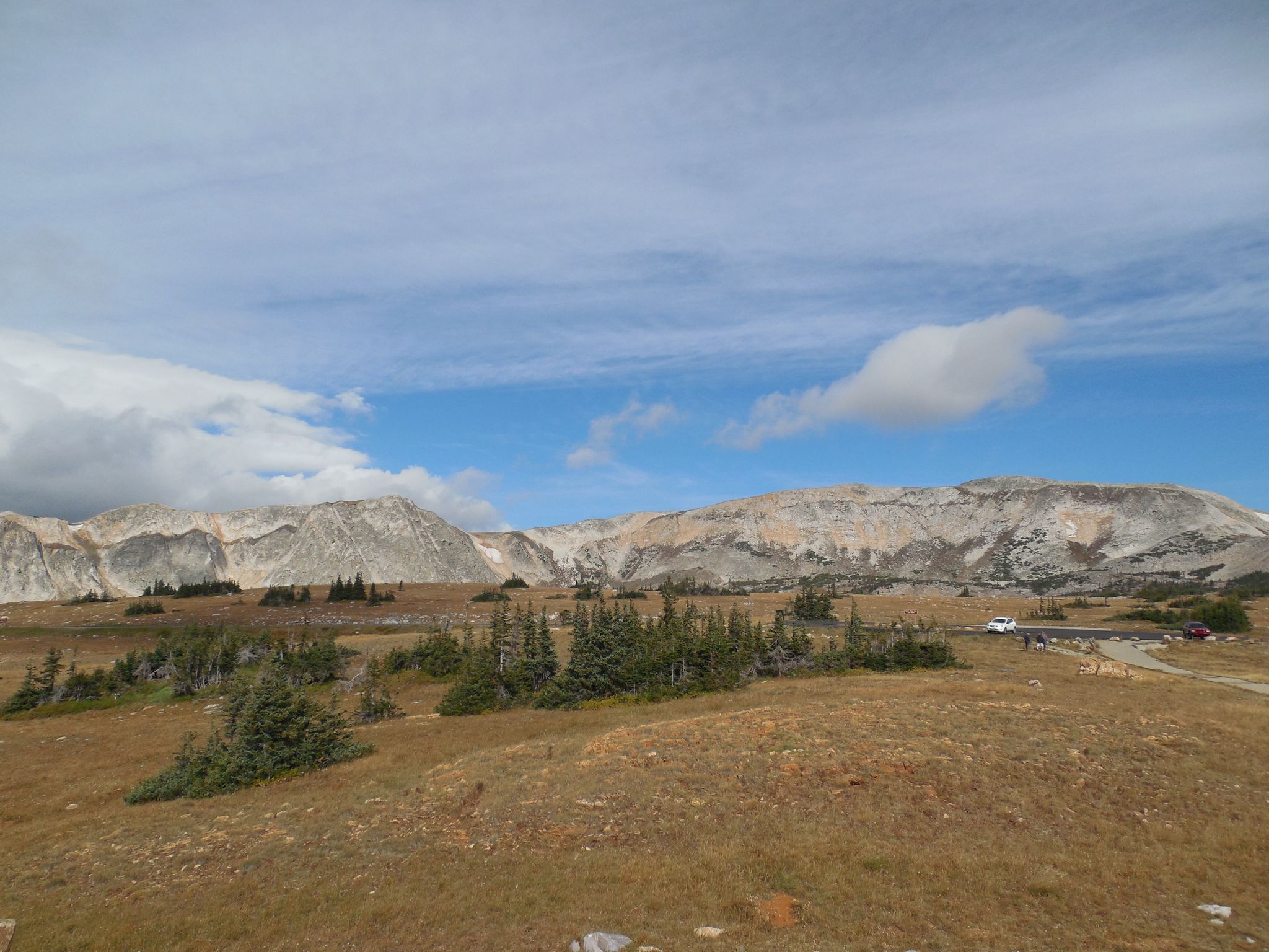 Vast, arid mountain landscape under a partly cloudy sky, with a distant vehicle. - Snowy Range Road (Lake Marie to Snowy Range Pass)