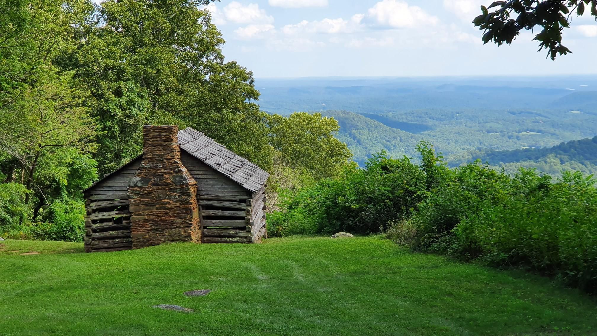 A rustic log cabin with a stone chimney overlooks a vast mountain range. - Smart View Loop Trail