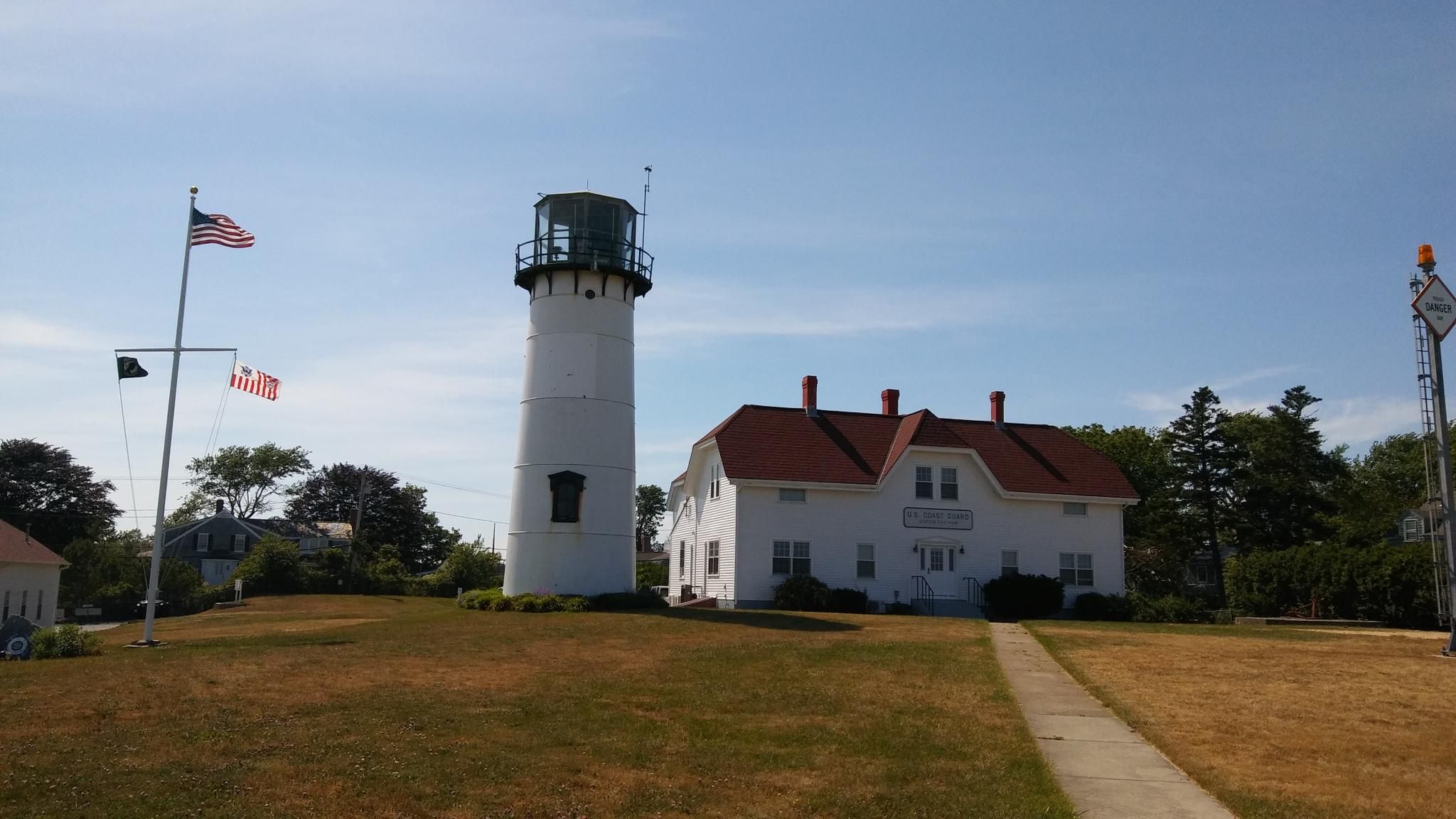 White lighthouse and house on a sunny day with flags flying. - Lighthouse Beach Trail