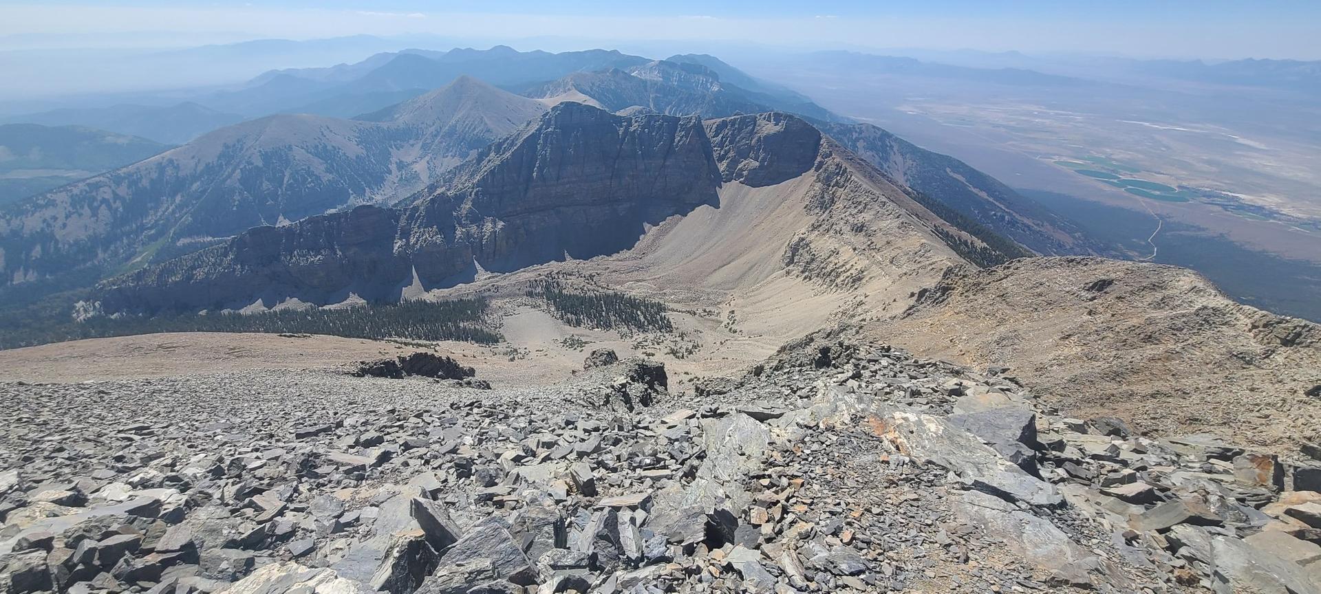 A panoramic view from a rocky peak shows vast mountains and a distant valley.
