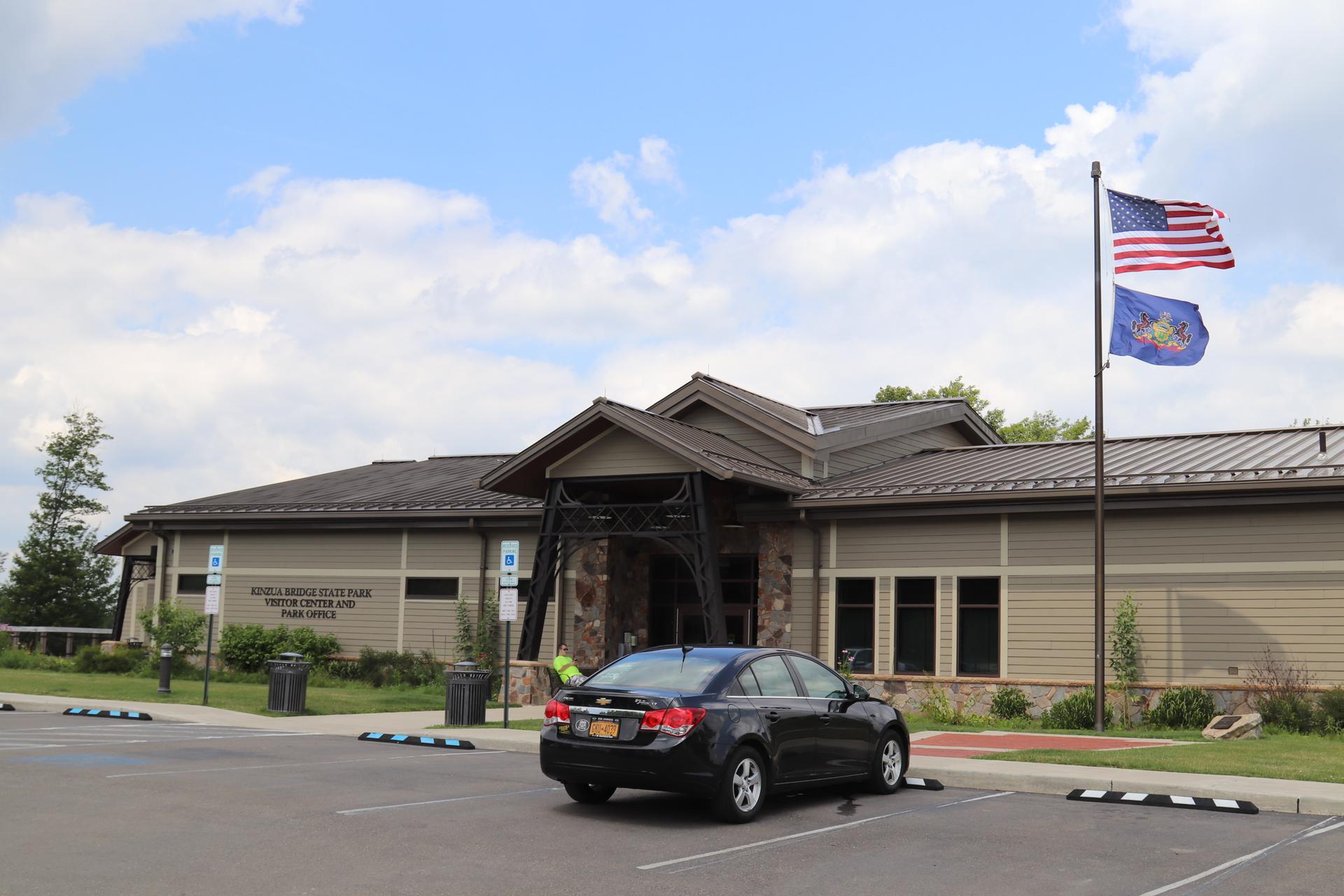 Modern building with flags flying, a black car parked on a sunny day.