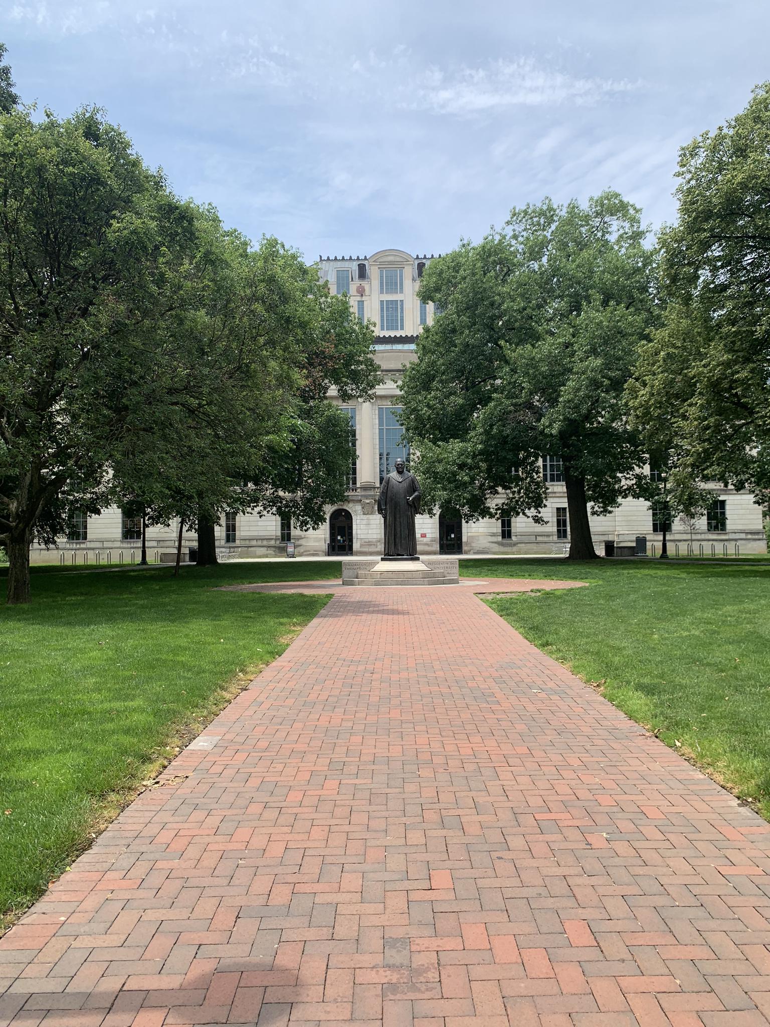 Brick path leads to a statue before a grand building under an overcast sky.
