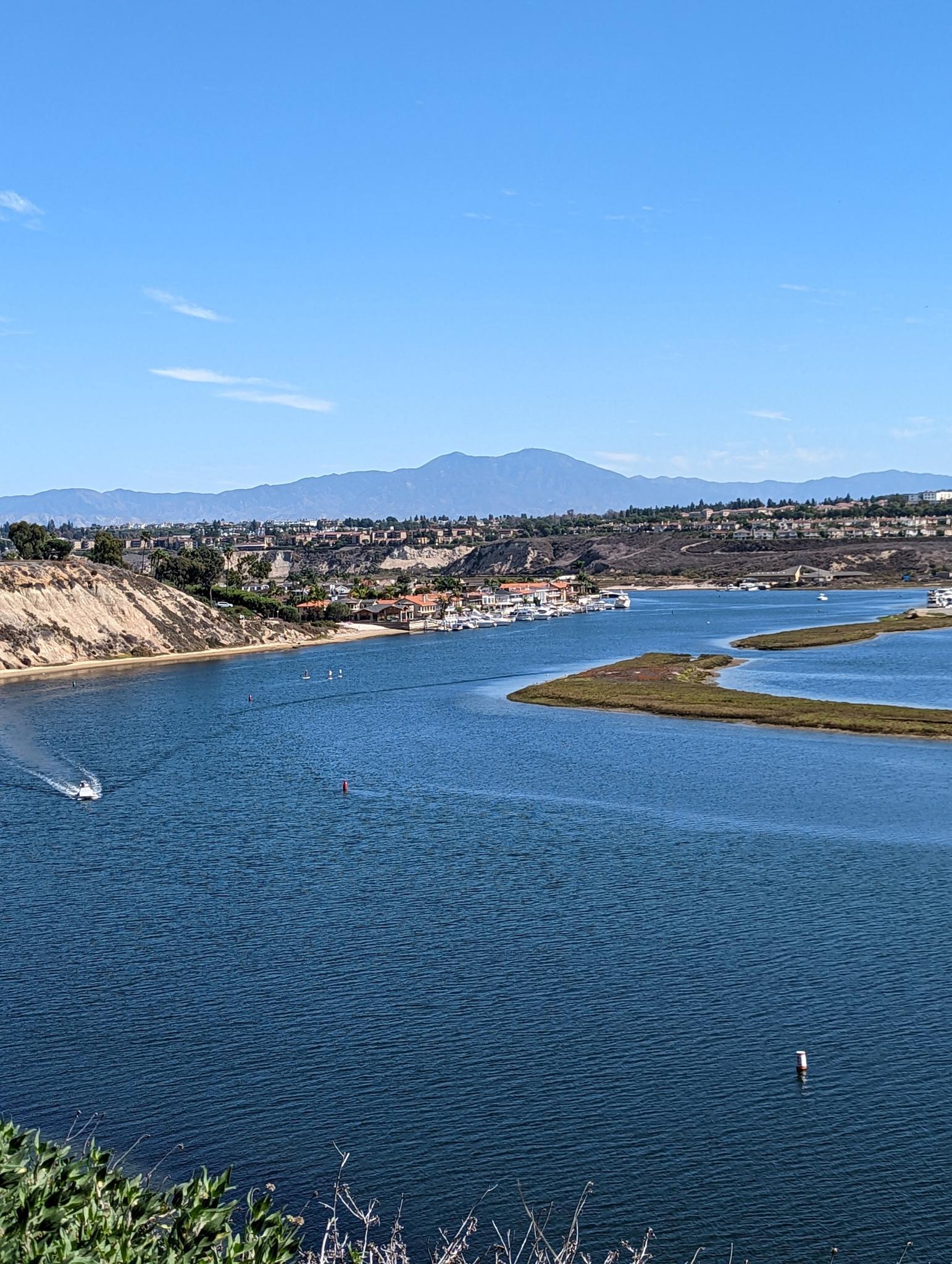 A wide blue bay with boats, coastal hills, and distant mountains.