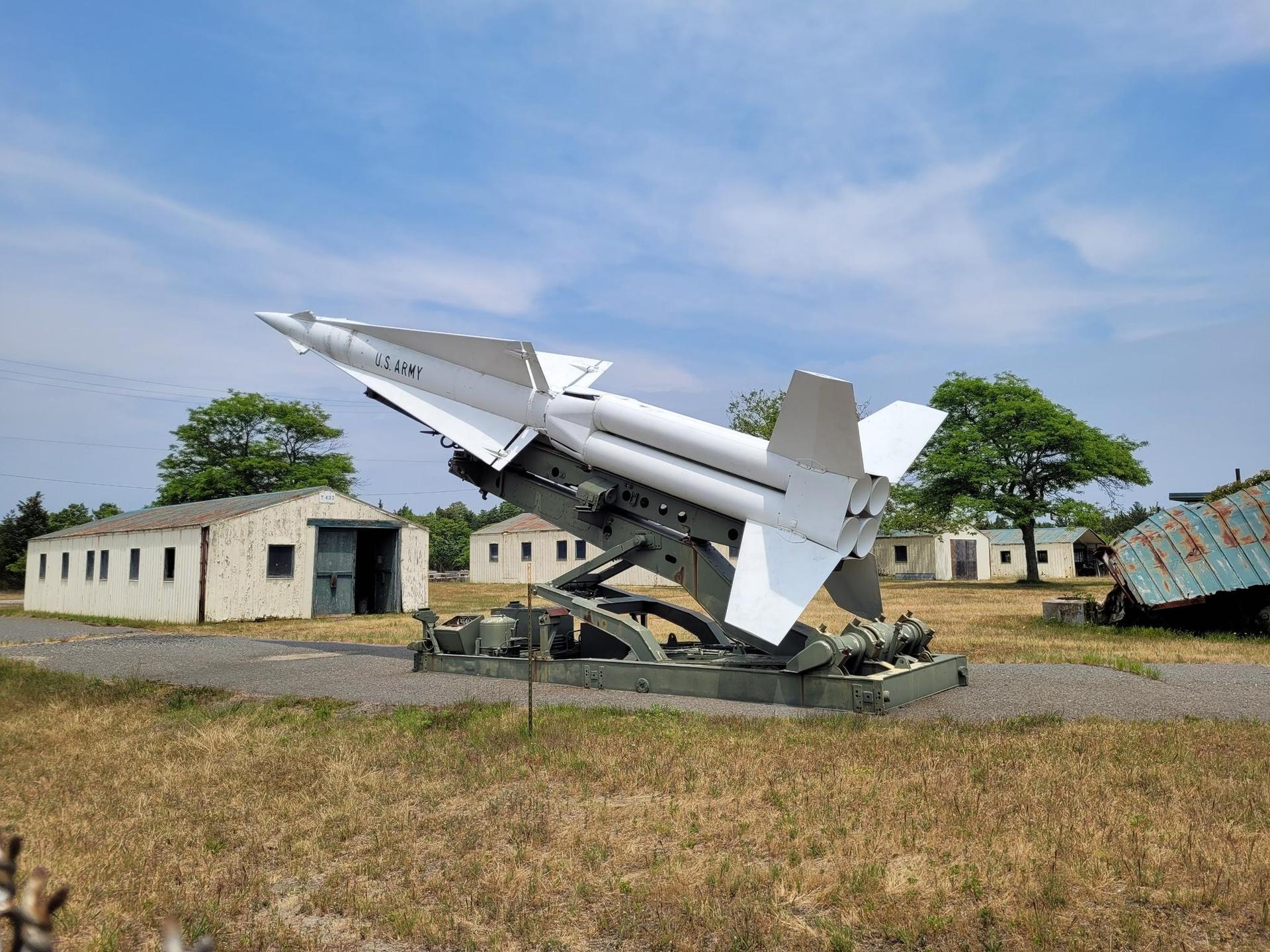 A large white missile on a launcher in a grassy field, sunny day.
