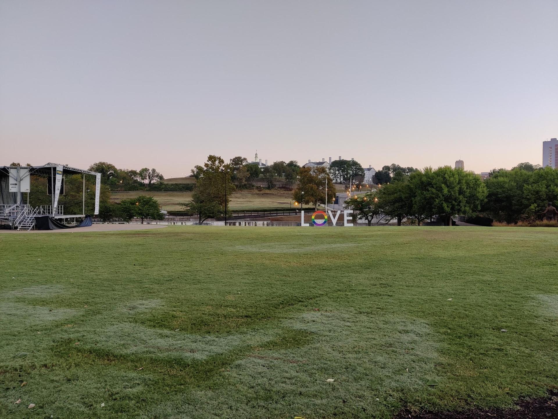 A wide grassy field with a 'LOVE' sign and distant buildings under soft light.