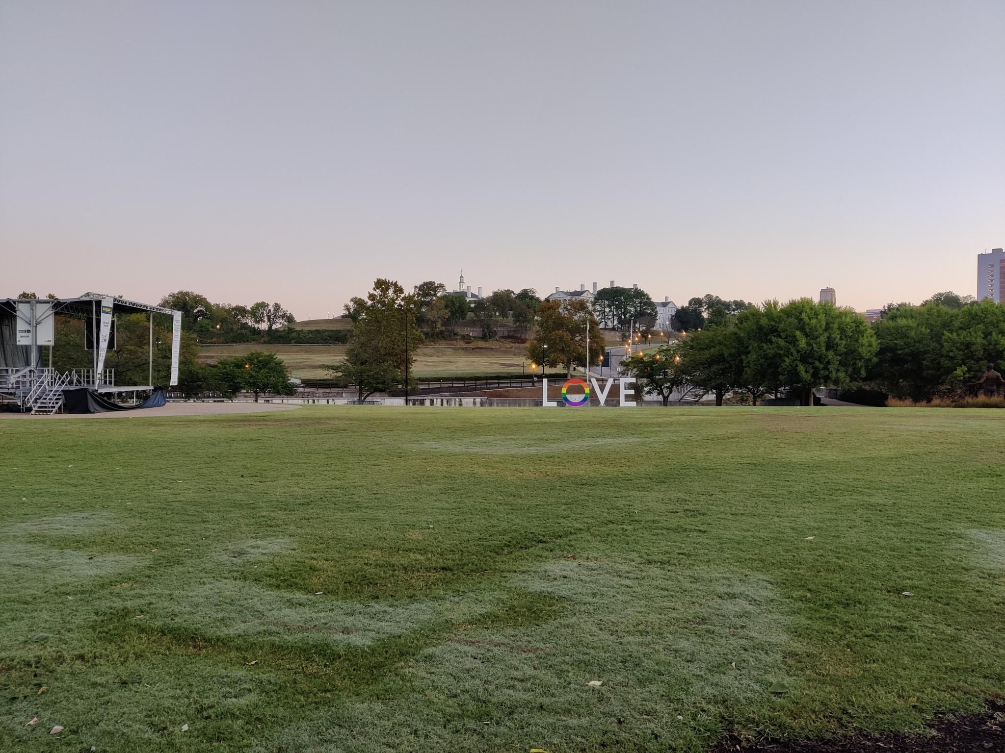 A wide grassy field with a 'LOVE' sign and distant buildings under soft light. - Virginia Capital Trail