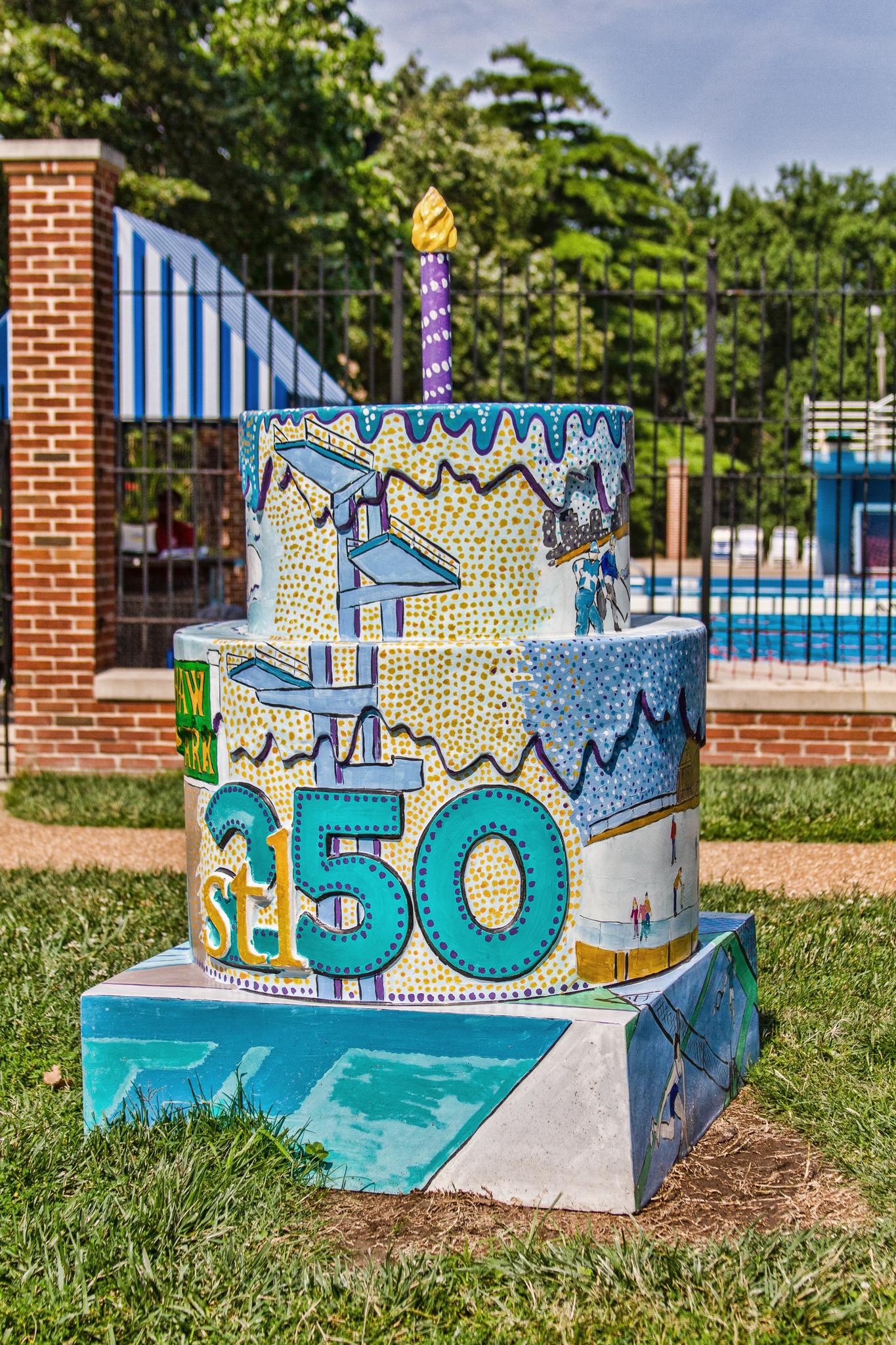 Large colorful outdoor cake sculpture with "350" on grass in bright daylight.