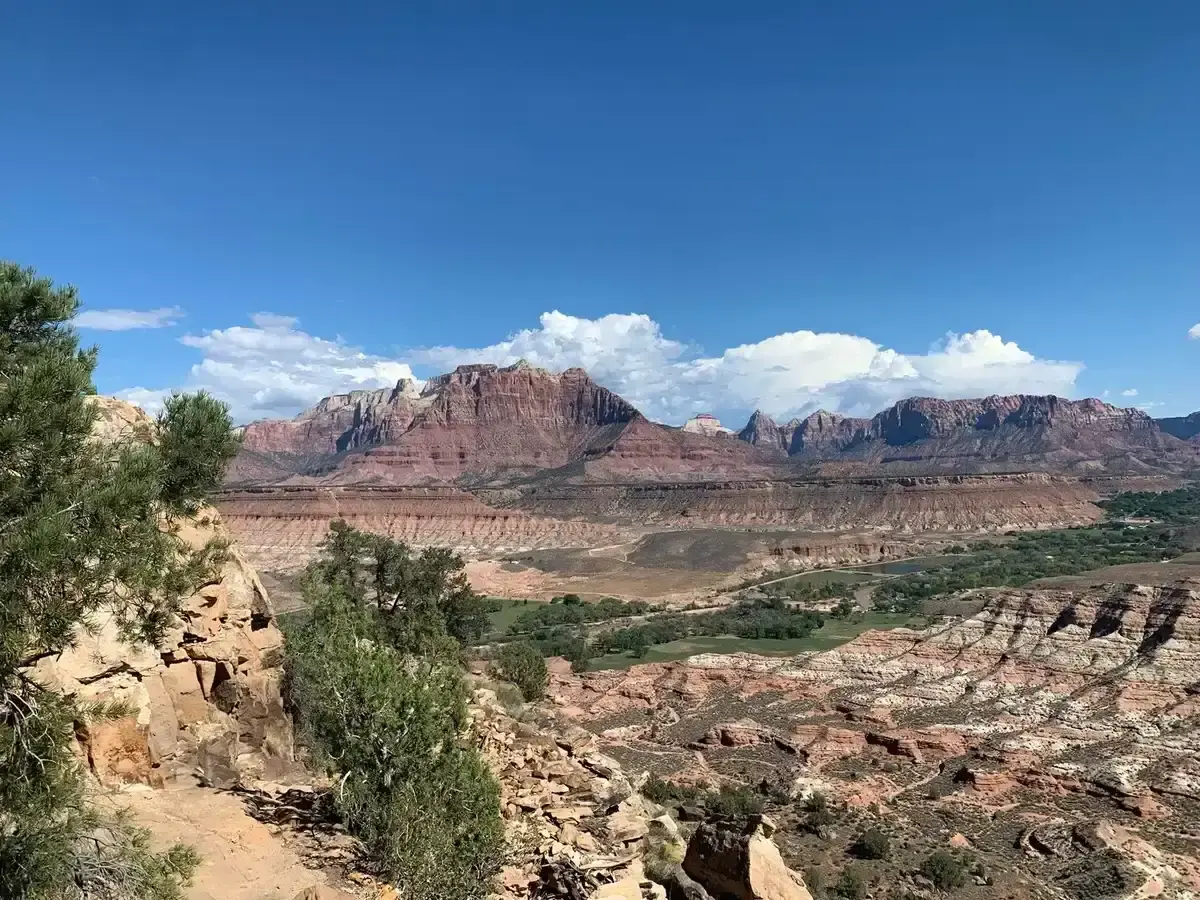 A vast desert canyon landscape with green valley and towering red mountains.