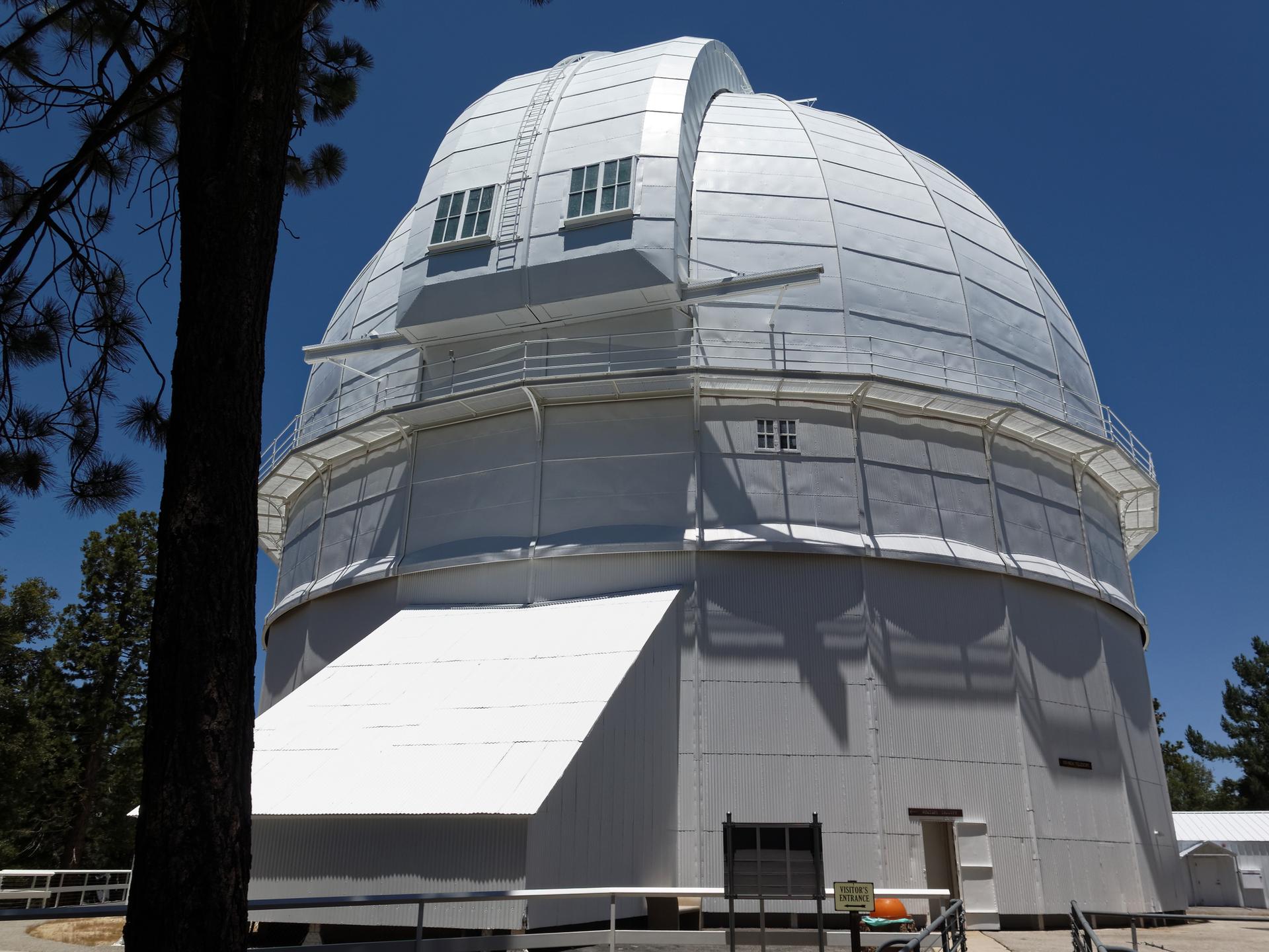 A large white observatory dome with balconies stands against a clear blue sky.