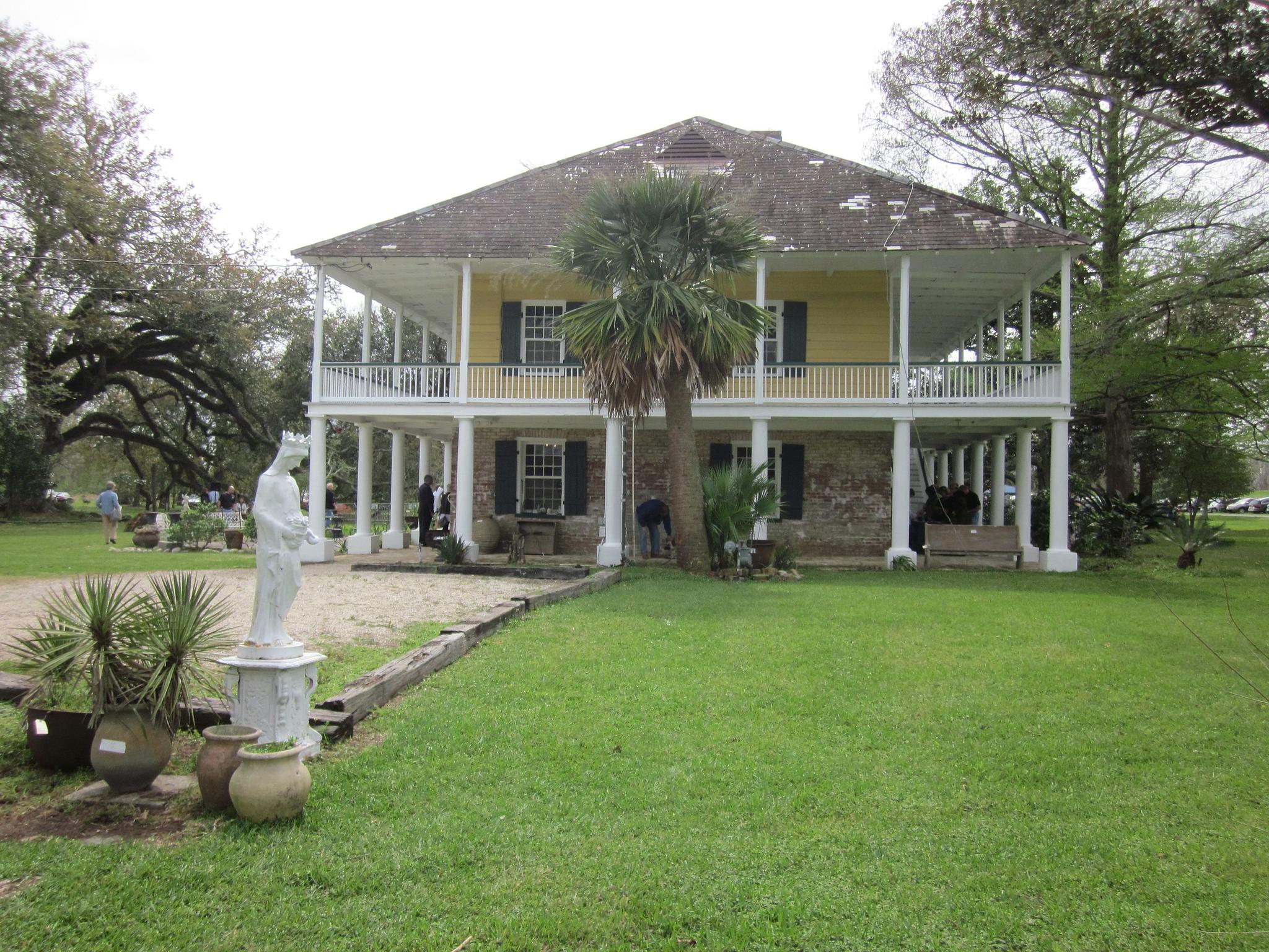 Large yellow house with double porches, palm tree, green lawn, cloudy day.