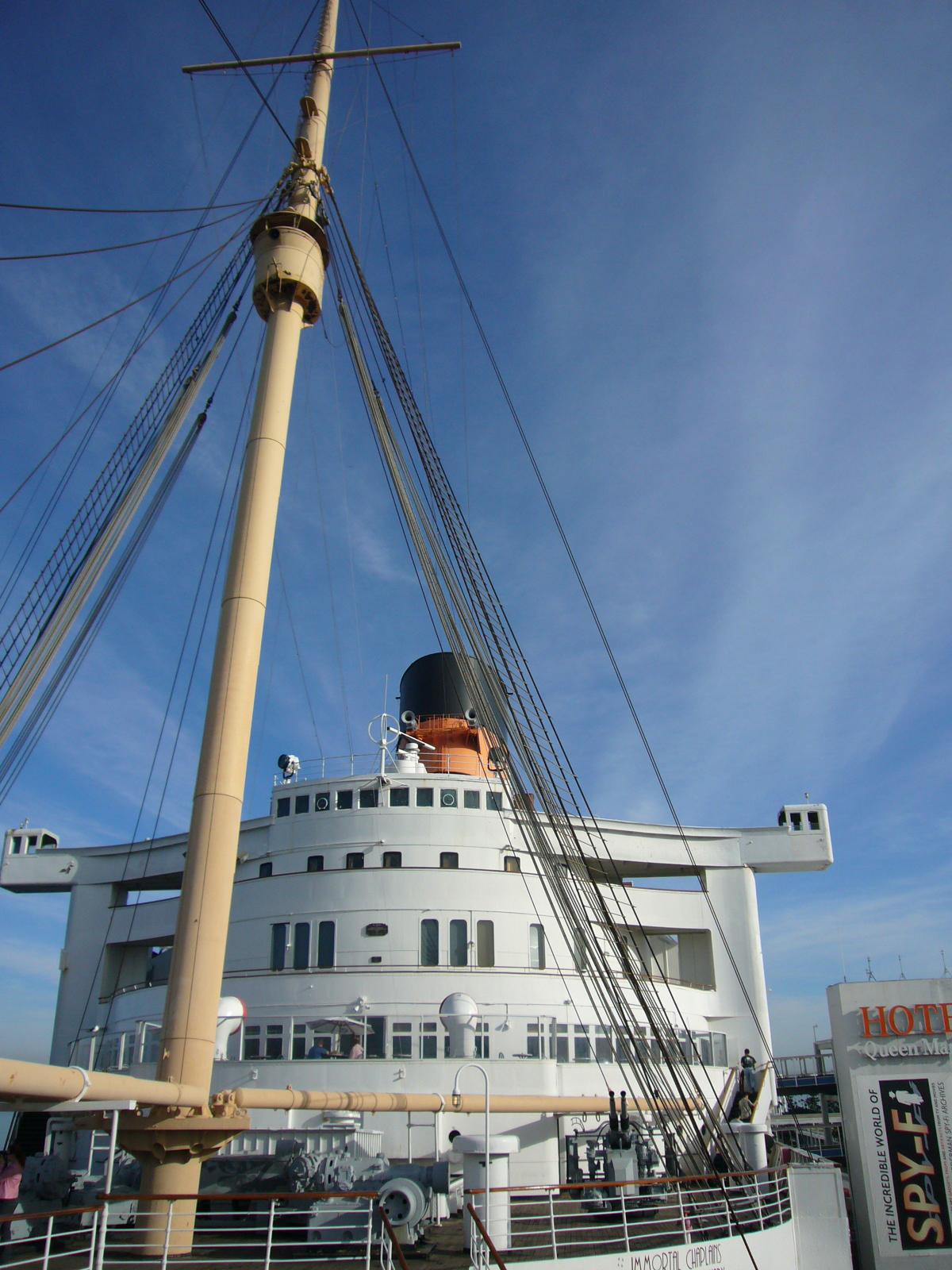 Tall mast and rigging of a large white ship against a bright blue sky.