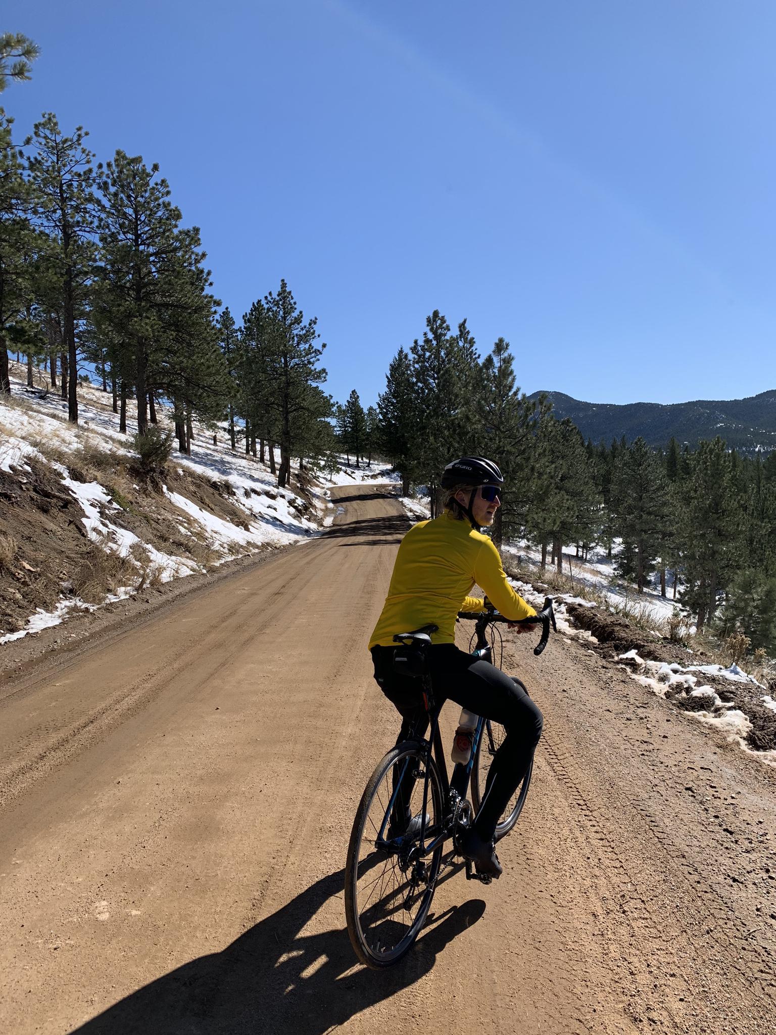 A person cycles on a dirt road through a snowy, forested landscape.