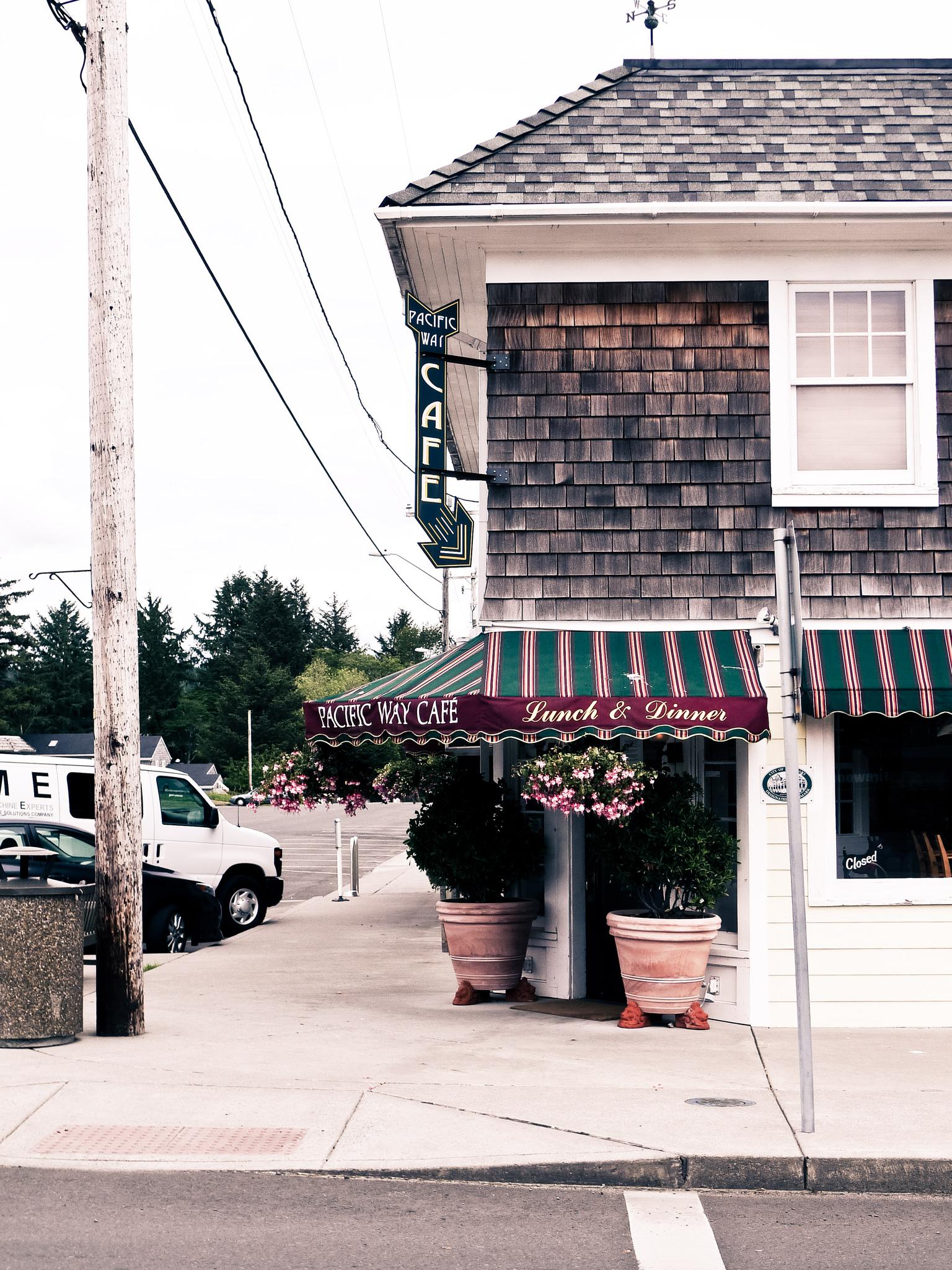 Quaint cafe building with striped awnings and hanging baskets on a street corner.